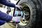 Osoba wymienia oponę pojazdu niebieskim kluczem udarowym w warsztacie.
