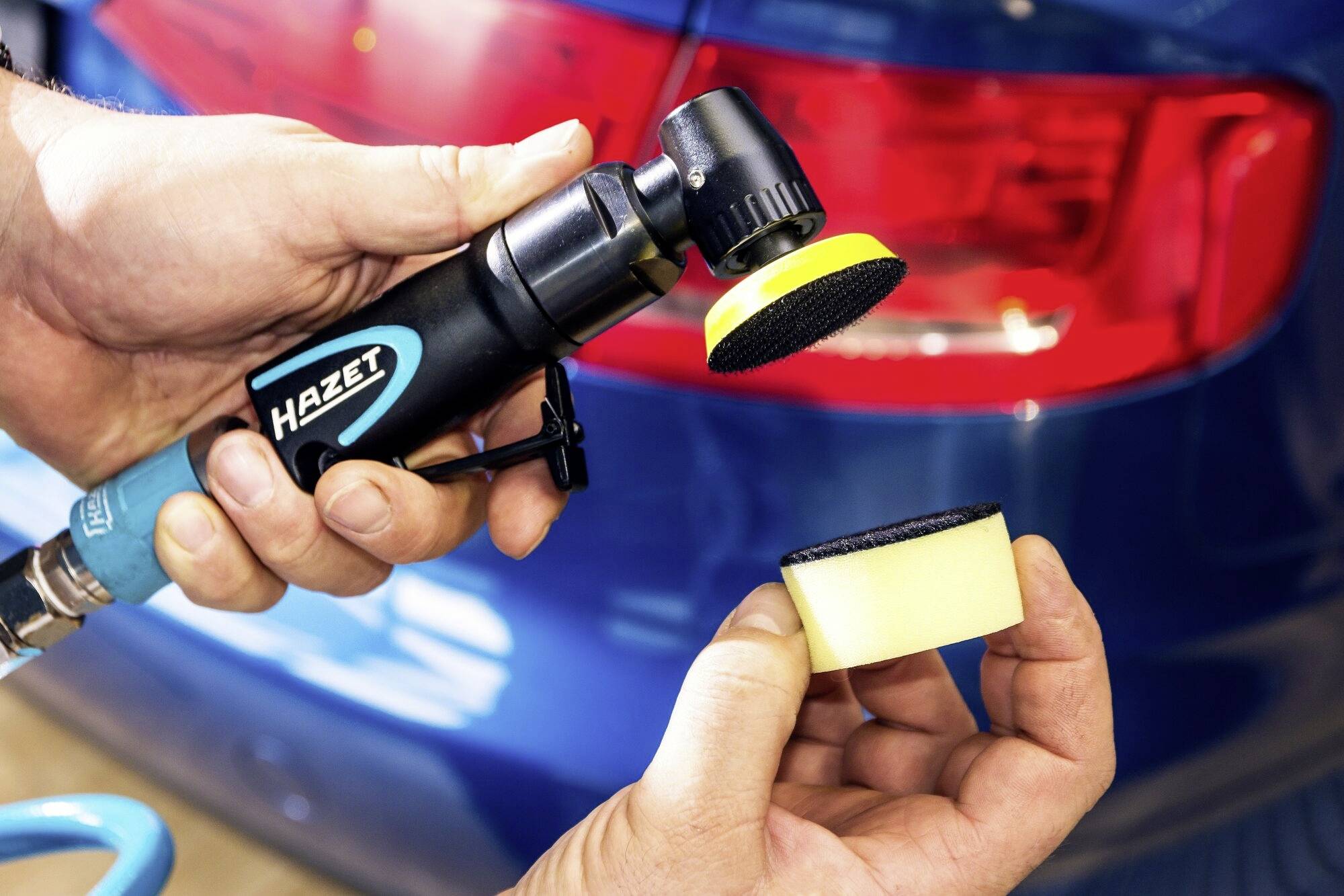 Zbliżenie dłoni trzymających maszynkę polerską i pady polerskie na tle niebieskiej lampy tylnej samochodu.