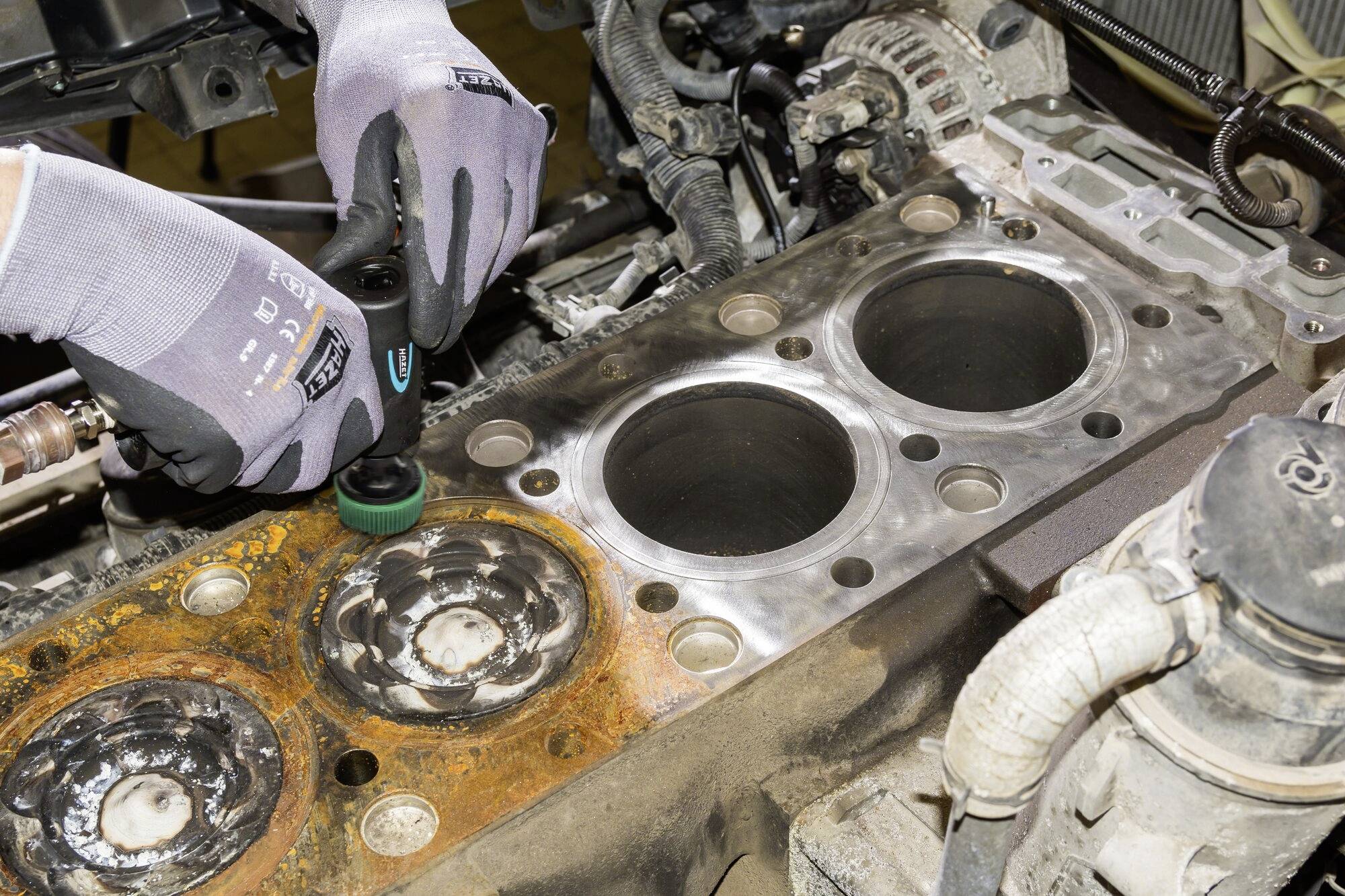 Osoba w szarych rękawiczkach czyści uszkodzony tłok w bloku silnika szczotką, usuwając rdzę.