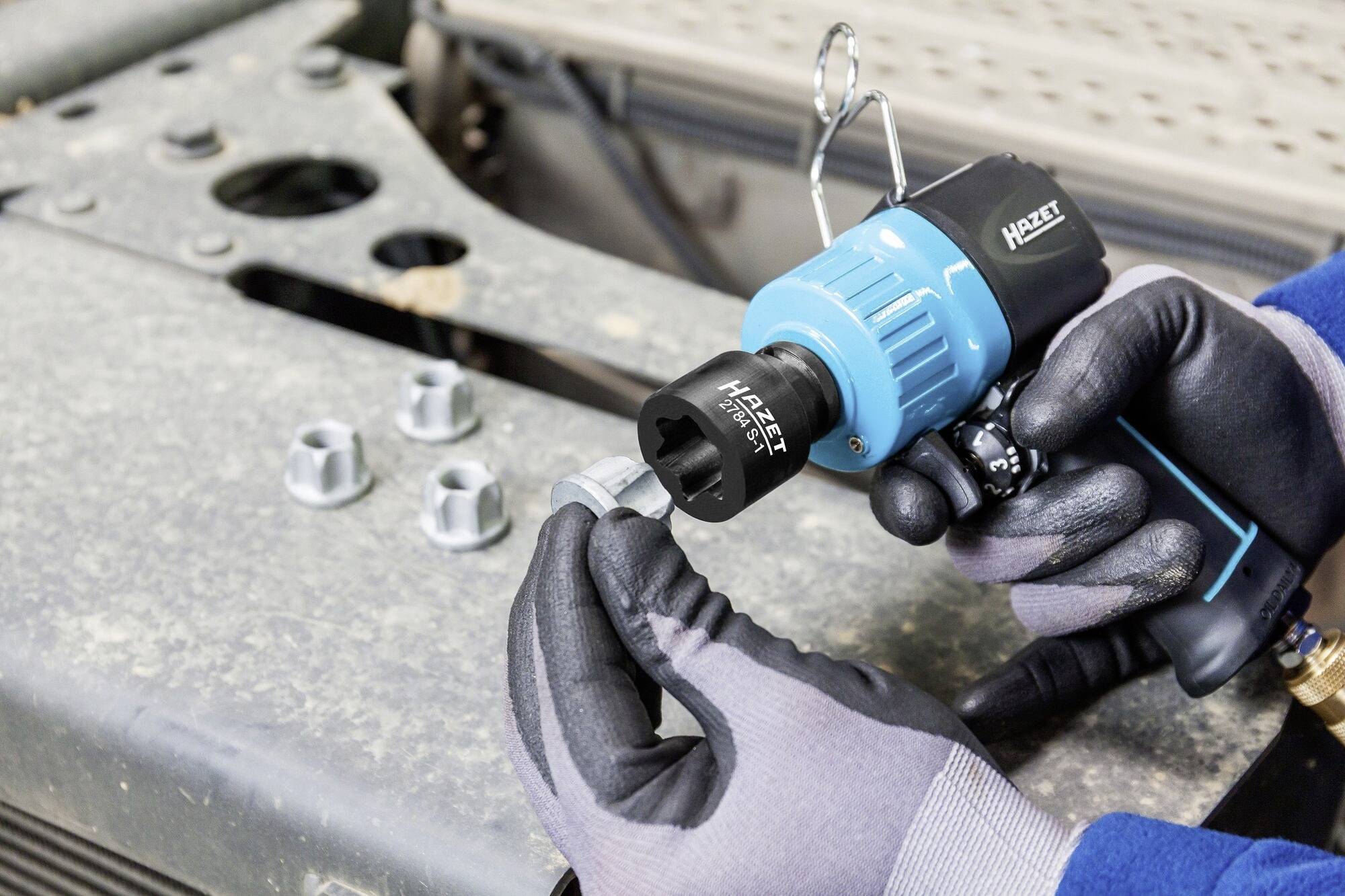 Osoba używa niebieskiego pneumatycznego klucza udarowego do zamocowania nakrętki na metalowej powierzchni.