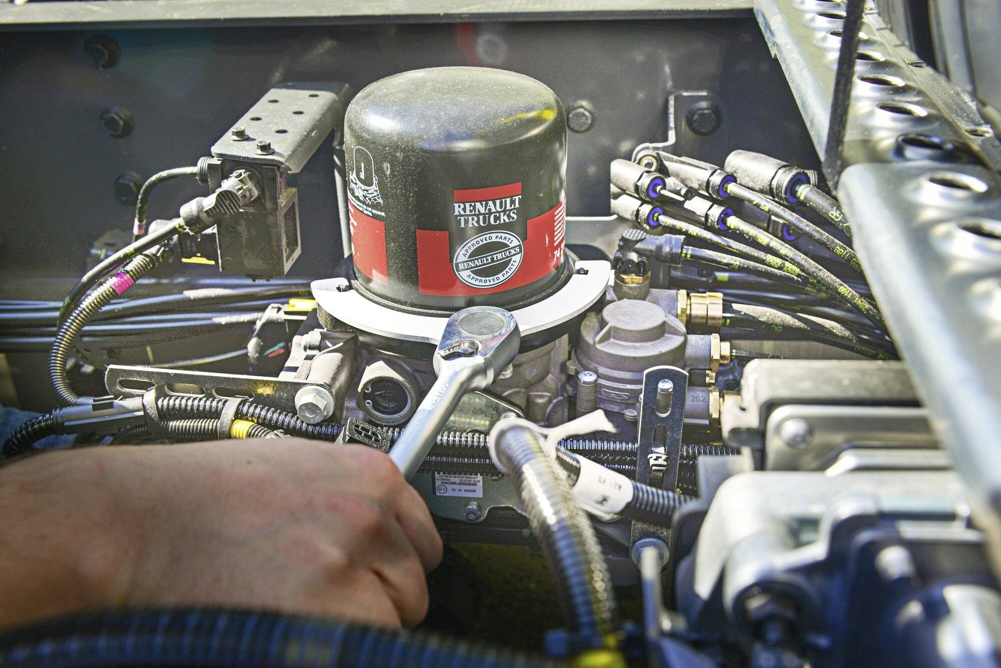 Mechanik dokręca śrubę kluczem w silniku maszyny Renault Trucks, otoczony kablami i przewodami.