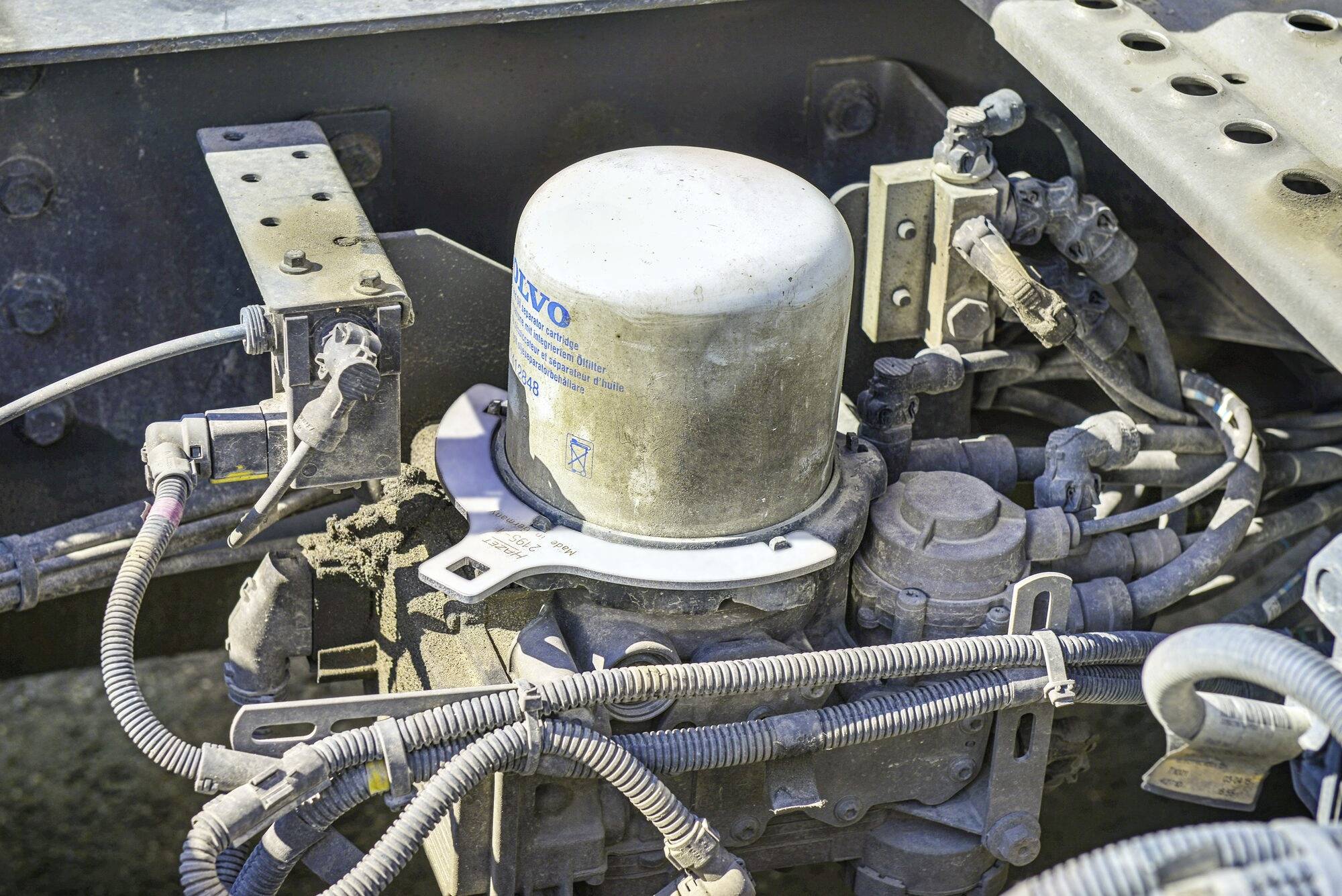 'Element systemu hamulcowego ciężarówki z wieloma przewodami i dużym cylindrycznym zbiornikiem w metalowej obudowie.'