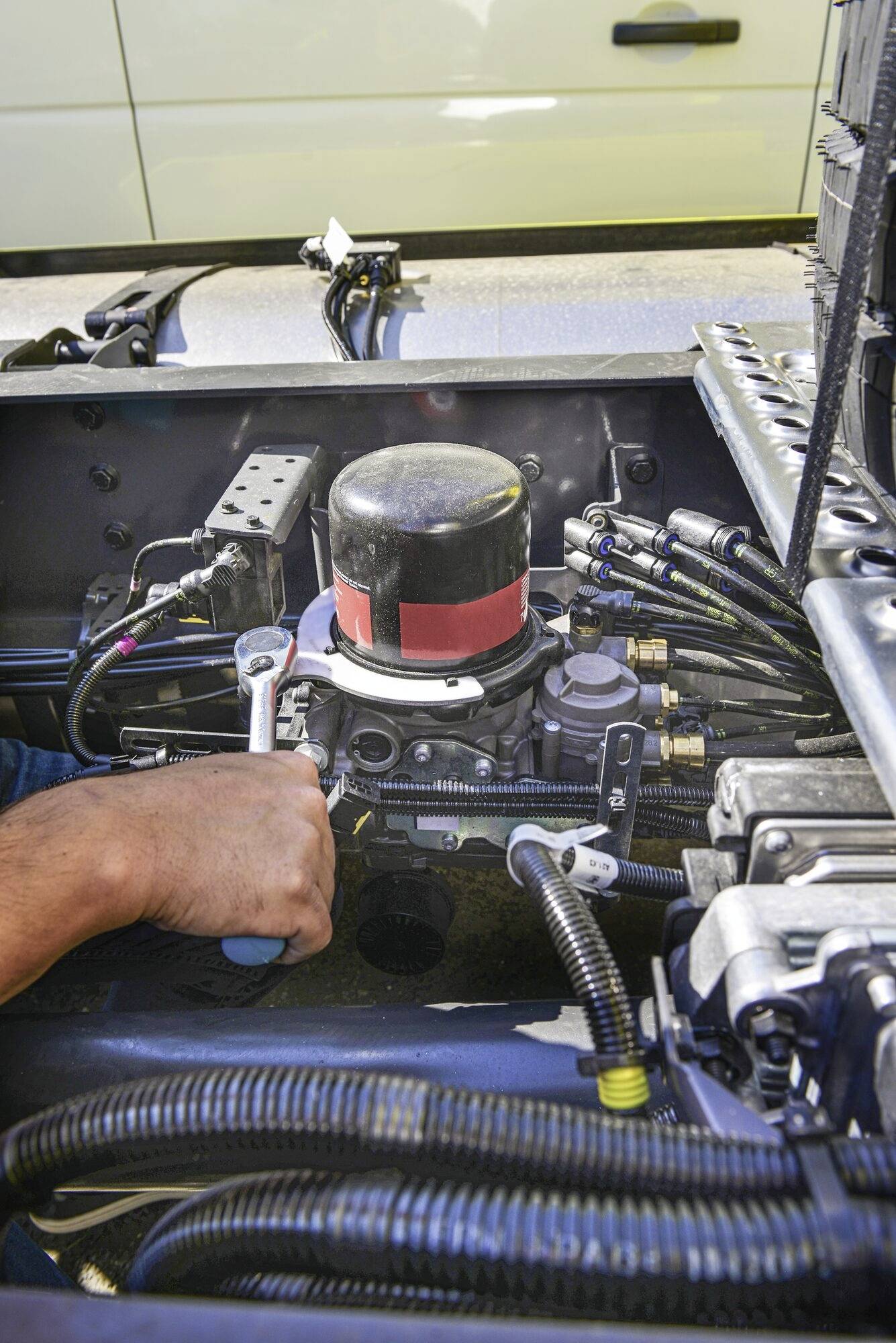 Osoba naprawia silnik pojazdu. Trzyma klucz w ręku i pracuje nad komponentem technicznym.