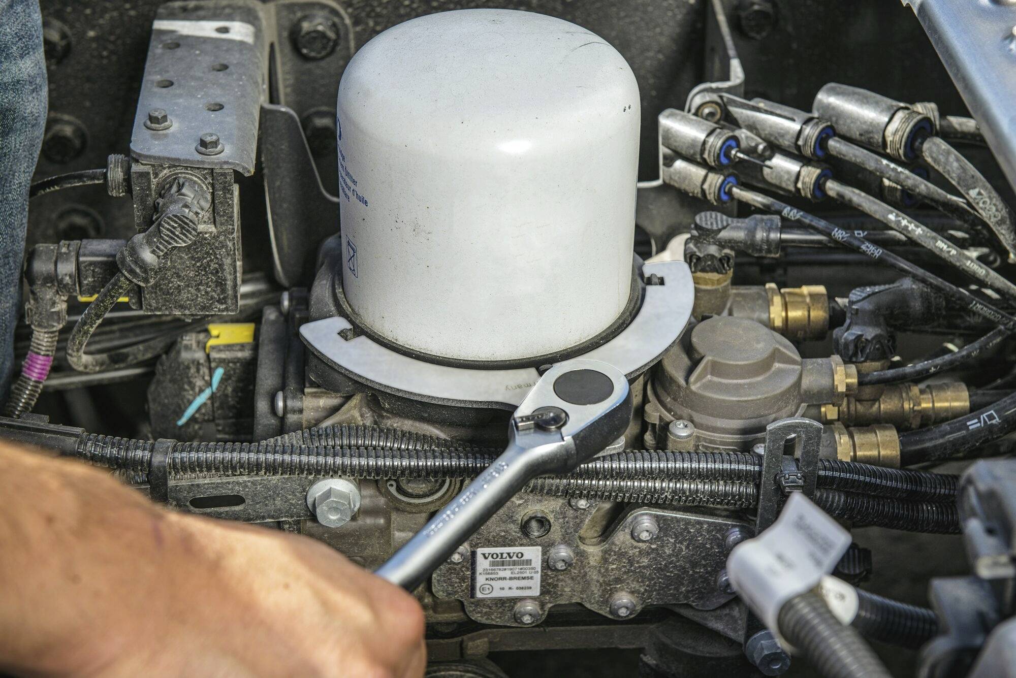 Człowiek używa klucza do konserwacji filtra w komorze silnika.