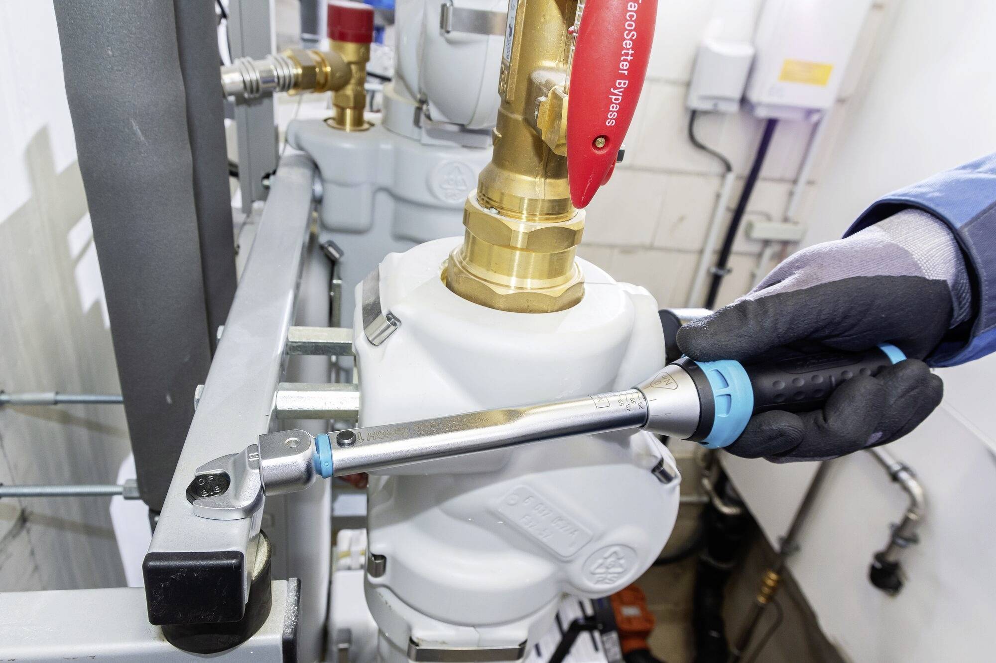 Osoba w rękawicach roboczych dokręca śrubę przy zaworze rurowym kluczem dynamometrycznym w pomieszczeniu technicznym.