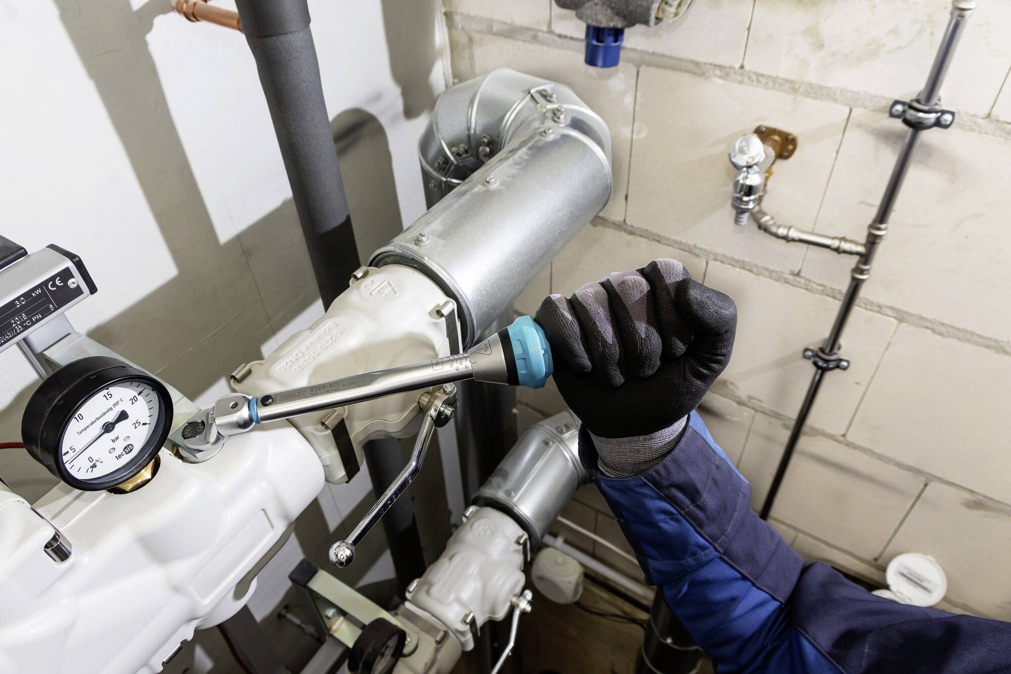 Rzemieślnik naprawia rurociąg w pomieszczeniu kotłowni, używając klucza na kołnierzu obok urządzenia pomiarowego ciśnienia.