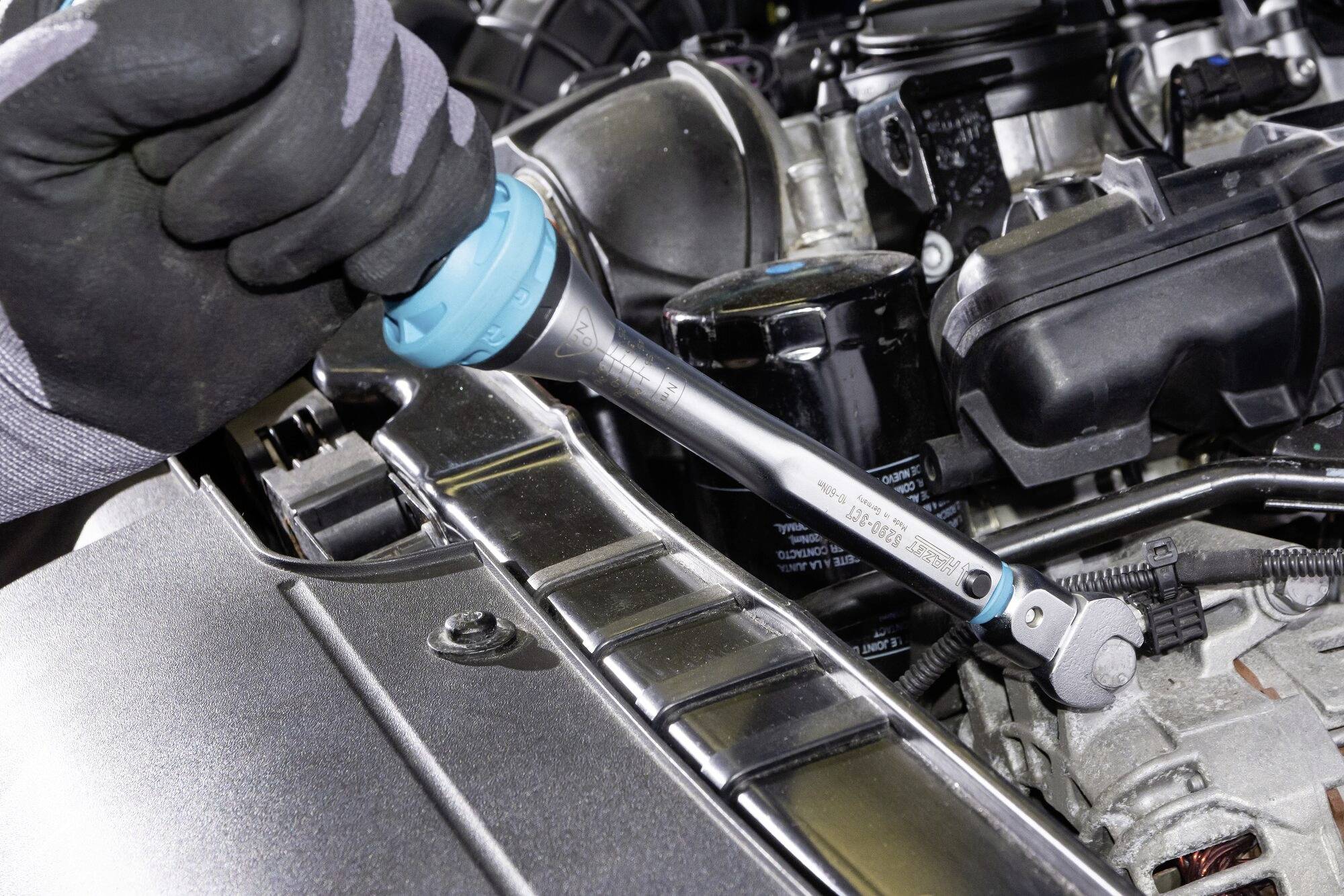 Ręka obraca kluczem dynamometrycznym śrubę w komorze silnika samochodu.