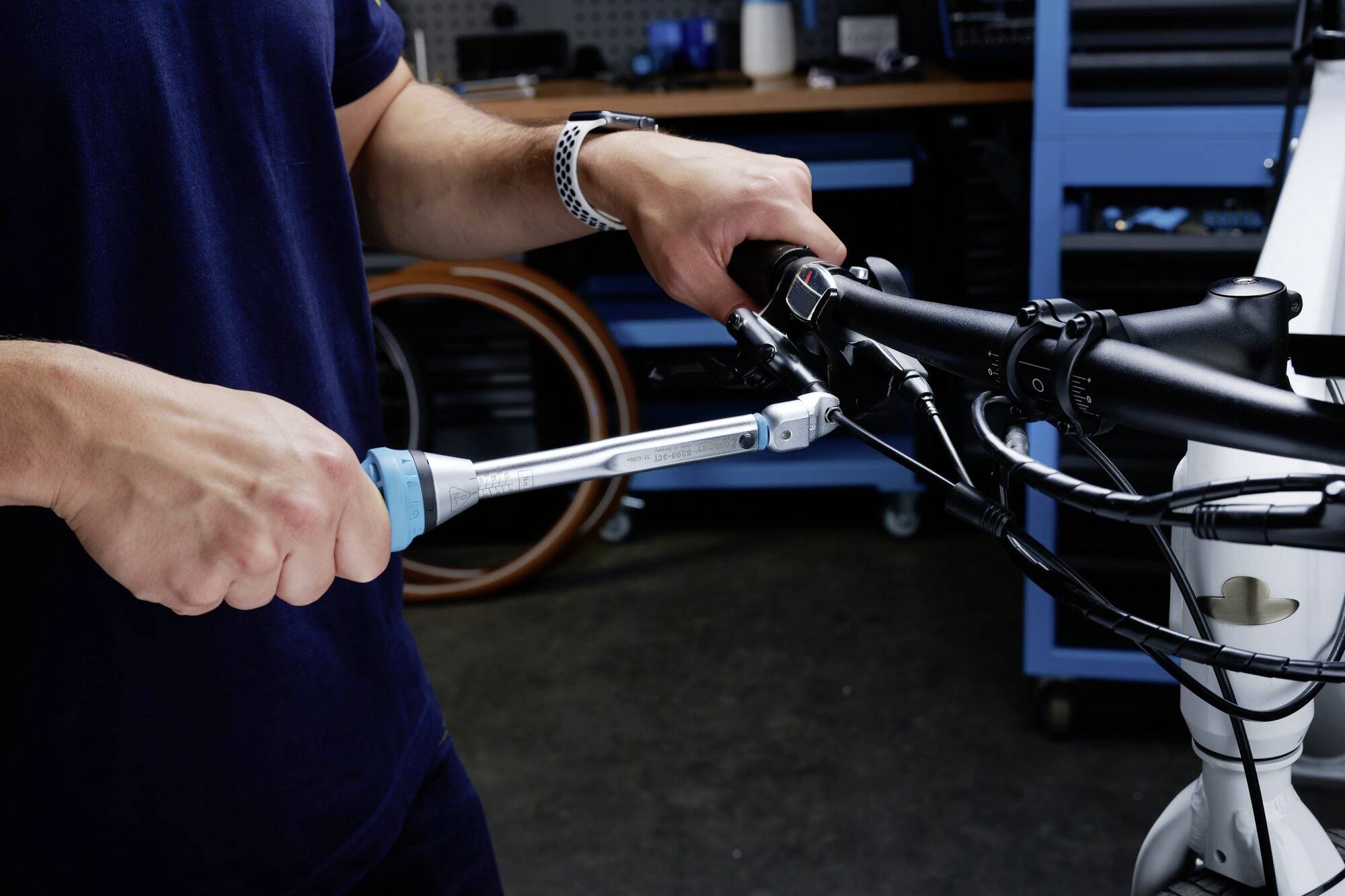 Osoba dokręca śrubę na kierownicy roweru kluczem dynamometrycznym. W tle widoczne są narzędzia.