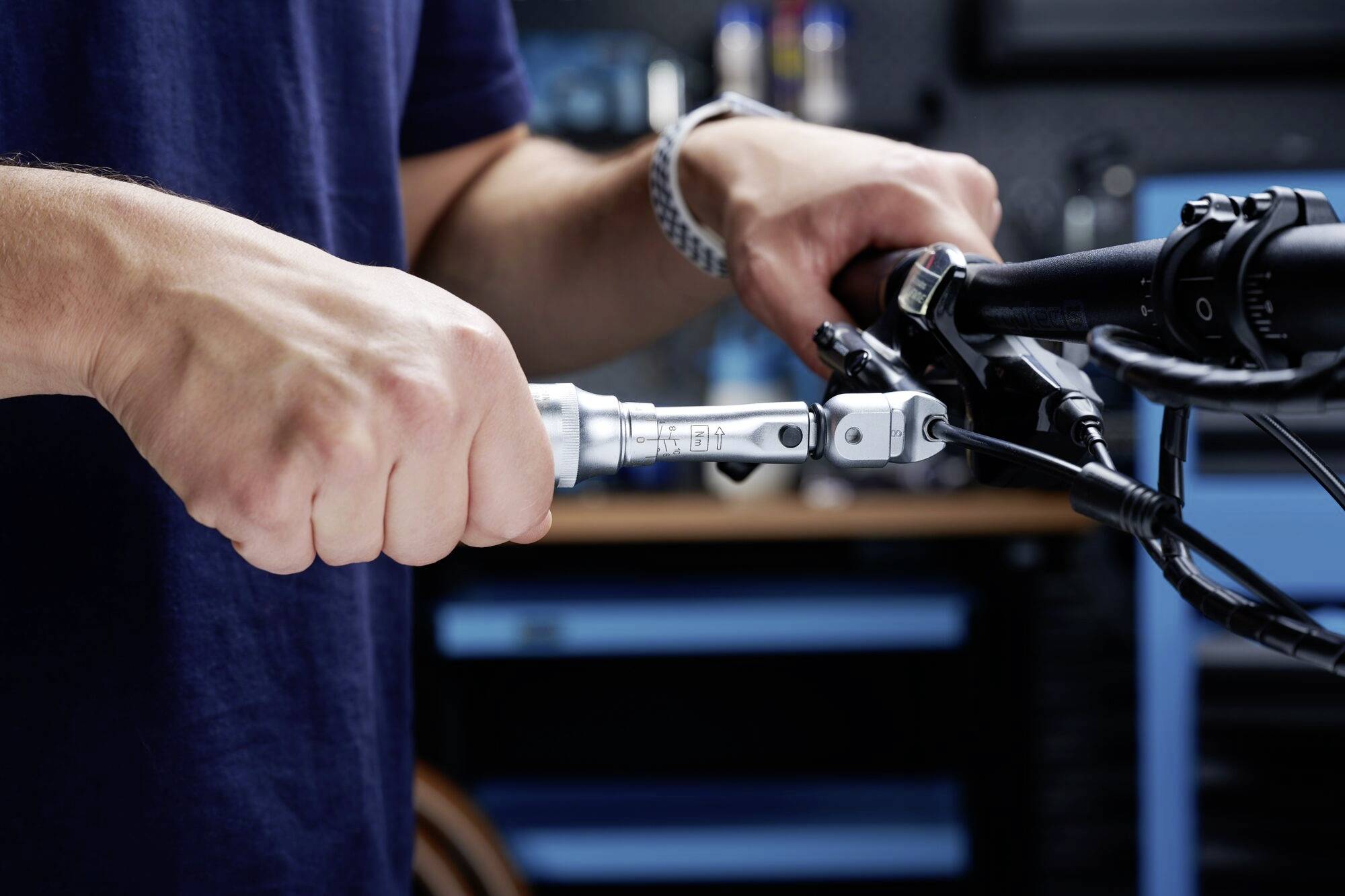 Osoba naprawia kierownicę roweru kluczem w warsztacie. Ręce skupione, w tle widoczny sprzęt techniczny.