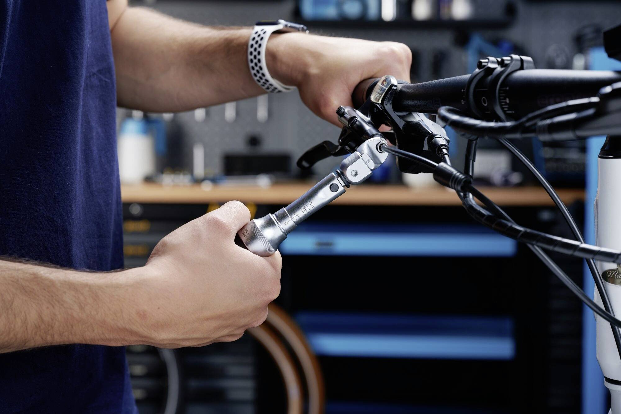Osoba za pomocą narzędzia reguluje kierownicę roweru w warsztacie. W tle widać rozmyte wyposażenie warsztatu.