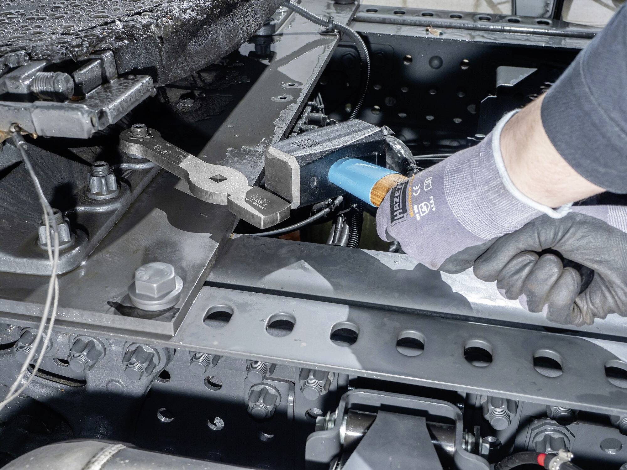 Osoba montuje przyczepę ciężarową kluczem i nosi przy tym rękawice robocze.