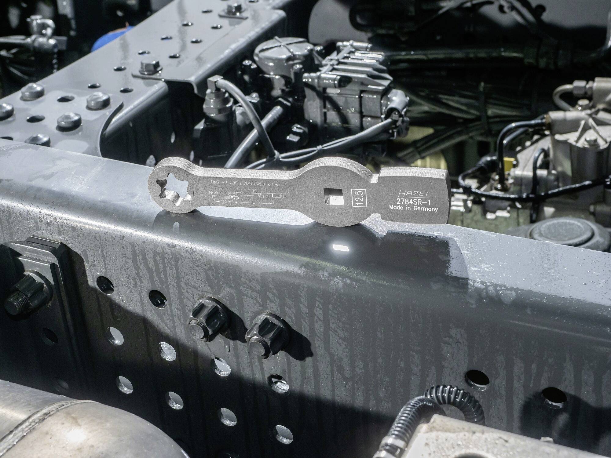 Metalowe narzędzie leży na elemencie pojazdu, z widocznym napisem 'HAZET 2795-1 Made in Germany'.