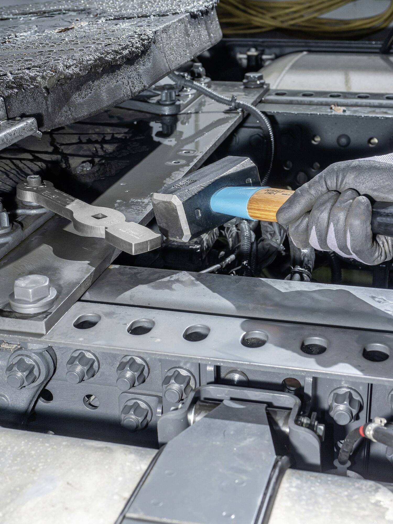 Mechanik mocuje zatrzask na odlewanym obrotowym podwoziu przyczepy za pomocą młotka.