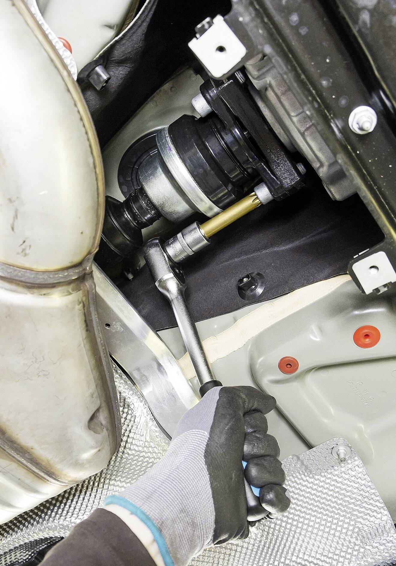 Osoba dokręca śrubę w części pojazdu za pomocą klucza. Zdjęcie przedstawia scenę naprawy w komorze silnika.