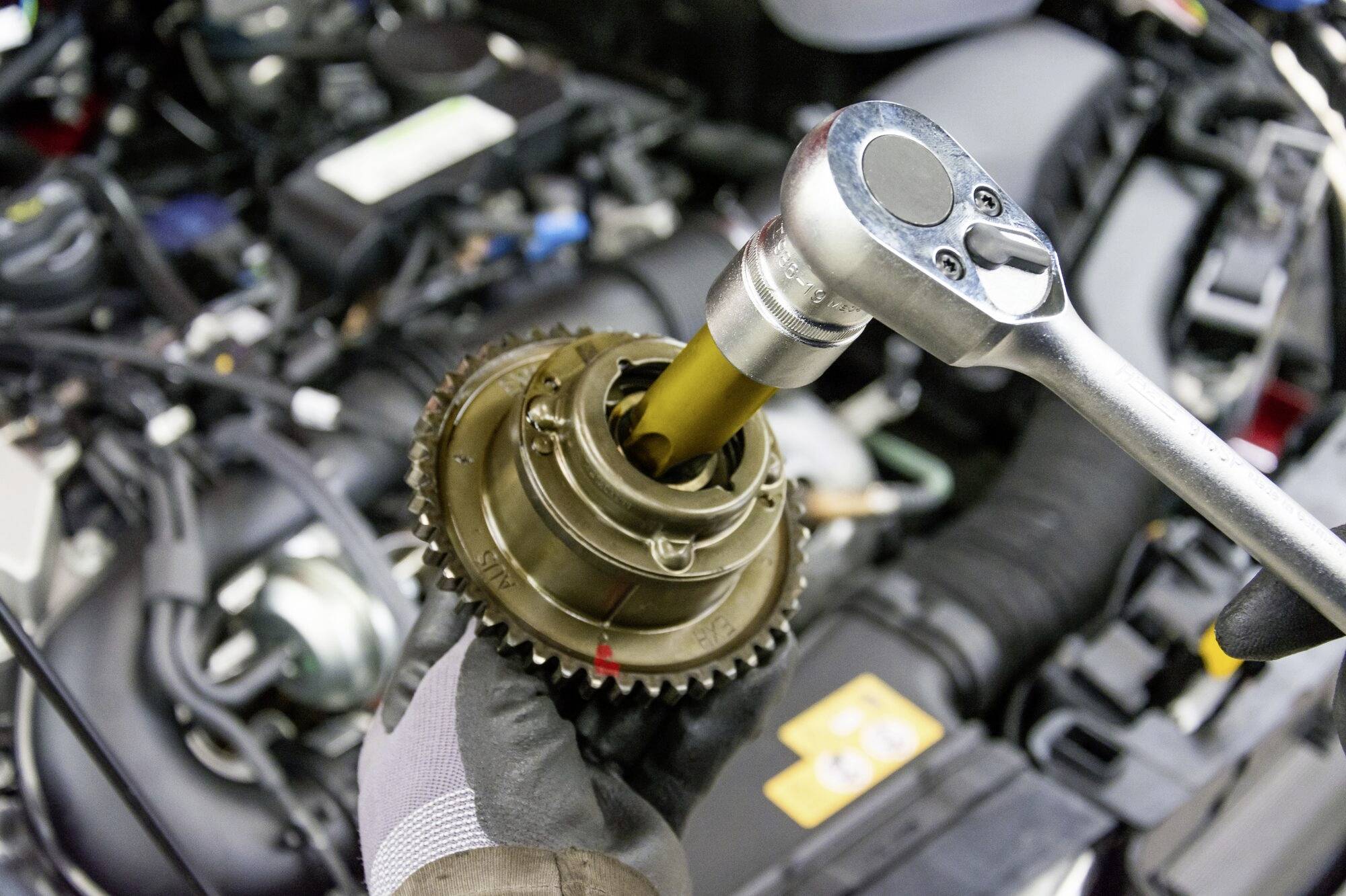 Mechanik wymienia część w komorze silnika samochodu za pomocą klucza. Silnik wygląda na czysty i dobrze utrzymany.