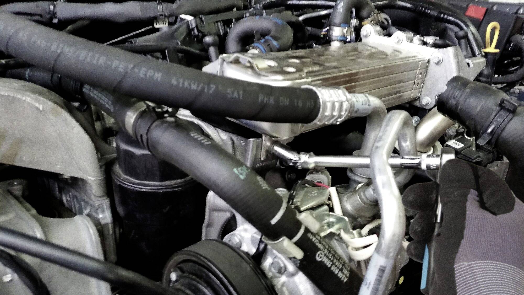 Element silnika z wieloma przewodami i elementami metalowymi, prawdopodobnie układ chłodzenia lub wentylacji w komorze silnika pojazdu.