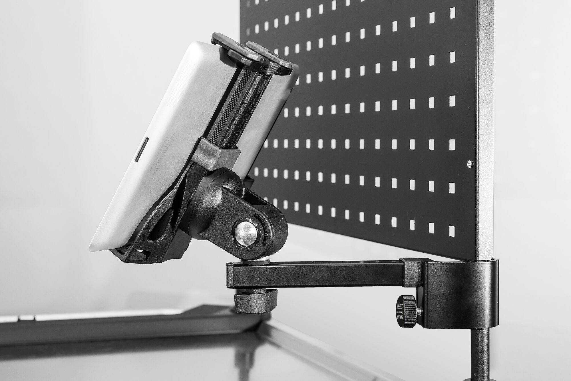 Tablet jest zamocowany w regulowanym uchwycie na tablicy perforowanej. Tło jest rozmyte.