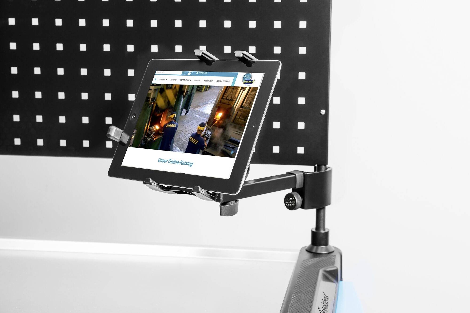 Tablet w uchwycie, wyświetlający stronę internetową z tytułem 'Nasz katalog online'. Tło: perforowana metalowa płyta.