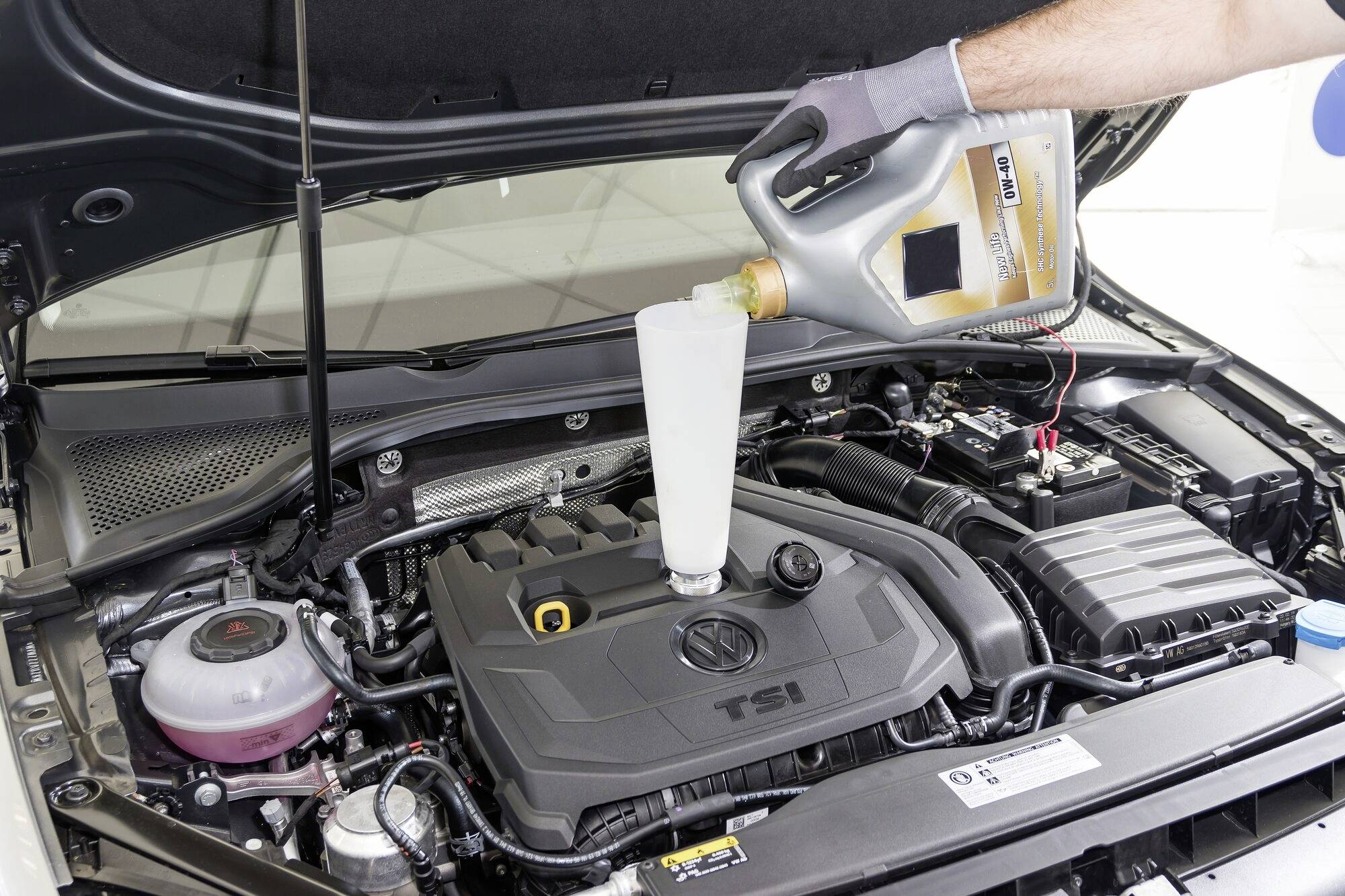 Mechanik wlewa olej do silnika samochodu. Widać komorę silnikową pojazdu, gdy olej jest wlewany przez lejek.