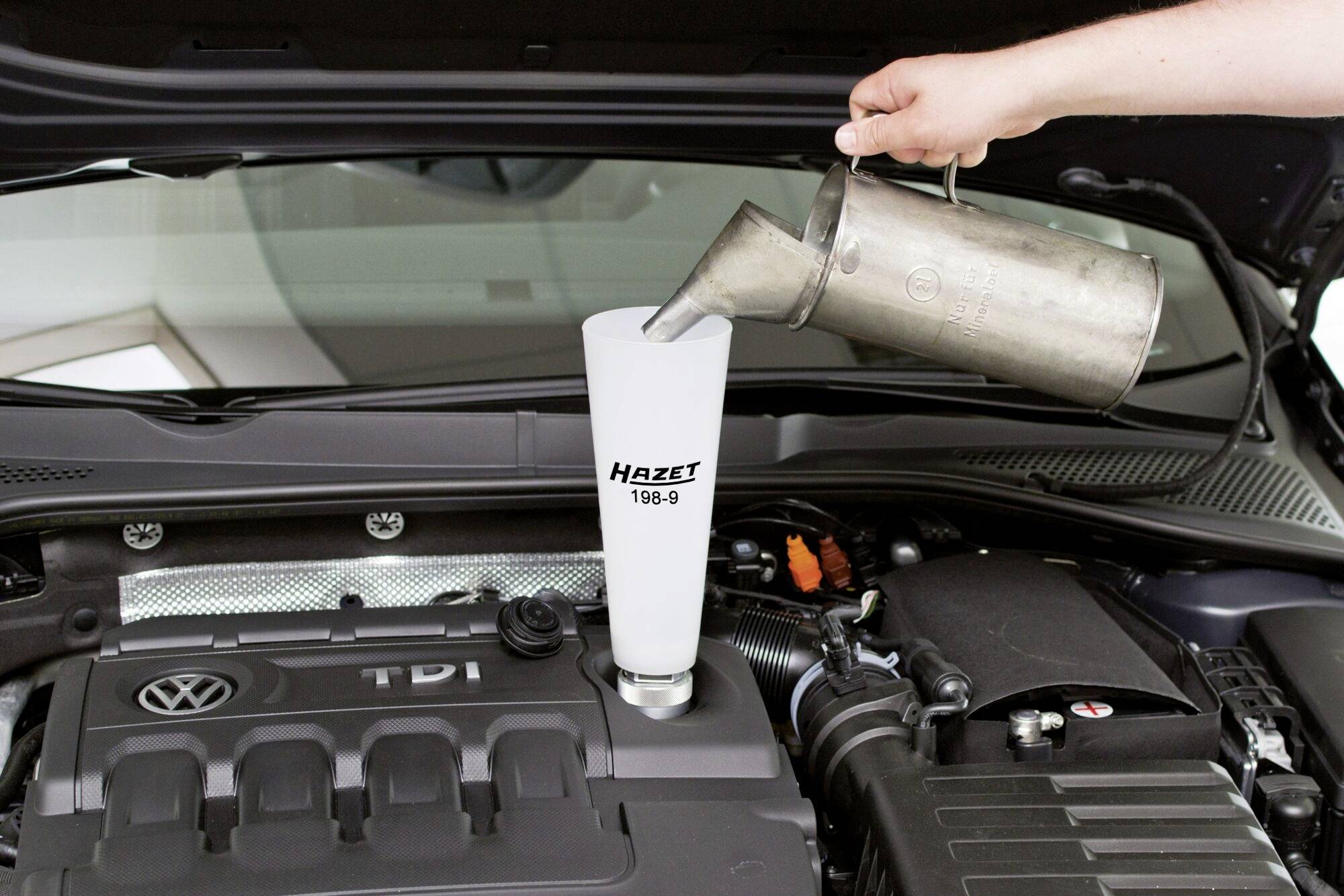 Osoba wlewa olej z metalowego kanistra do silnika samochodu. Silnik jest marki Volkswagen z logo 'TDI'.
