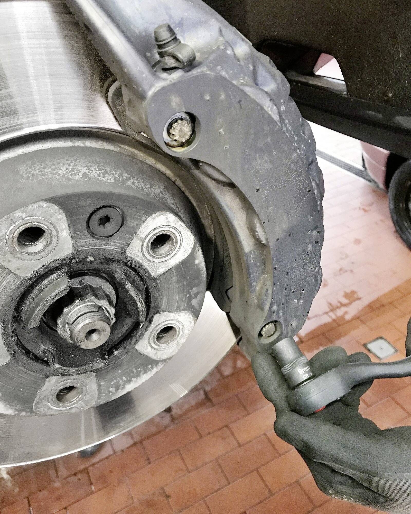 Zbliżenie mechanika naprawiającego tarczę hamulcową za pomocą narzędzi. Ostrość kadru skupiona jest na samej tarczy hamulcowej i wykonywanej czynności naprawczej.