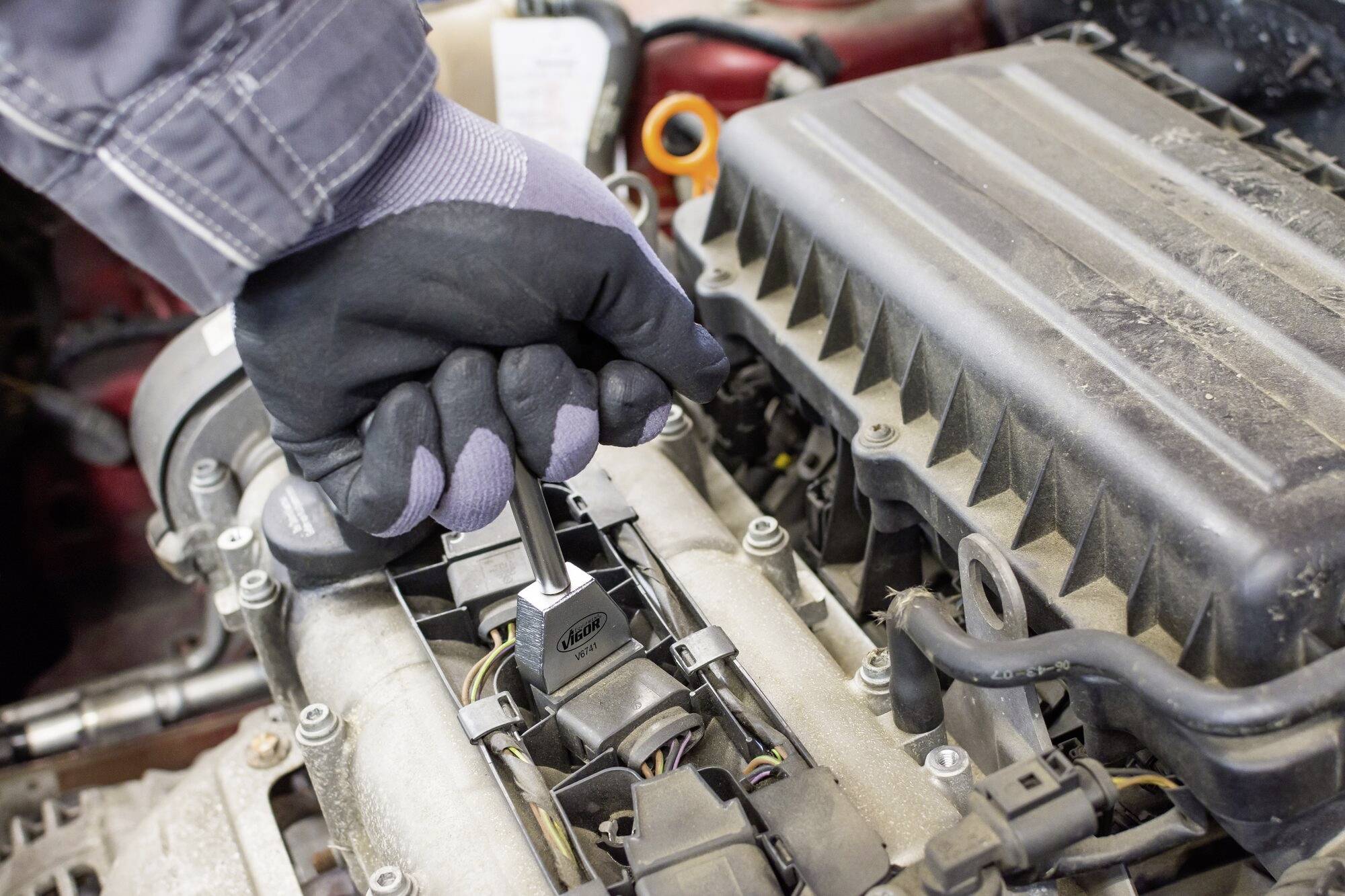 Zbliżenie dłoni w rękawicy roboczej, używającej klucza do pracy przy silniku samochodu.