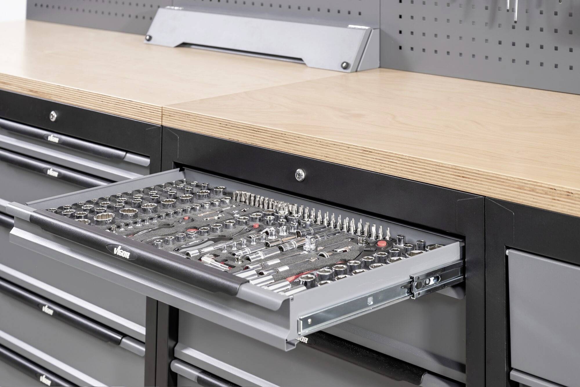 Otwarta szuflada szafki narzędziowej prezentuje liczne, starannie ułożone narzędzia ręczne, w tym klucze nasadowe i śrubokręty.