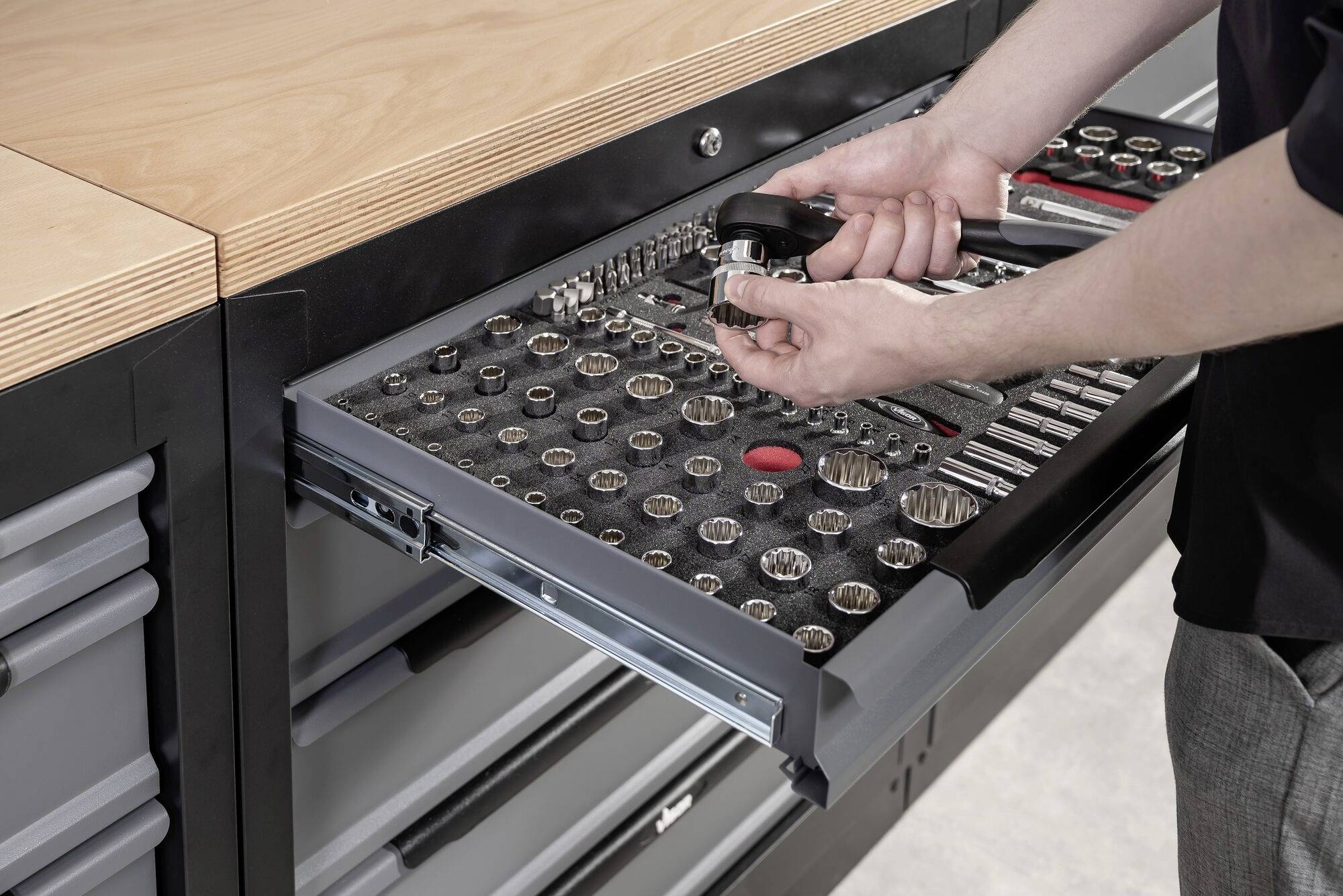 Osoba otwiera szufladę z różnymi narzędziami w warsztacie. Trzyma w ręku klucz nastawny.