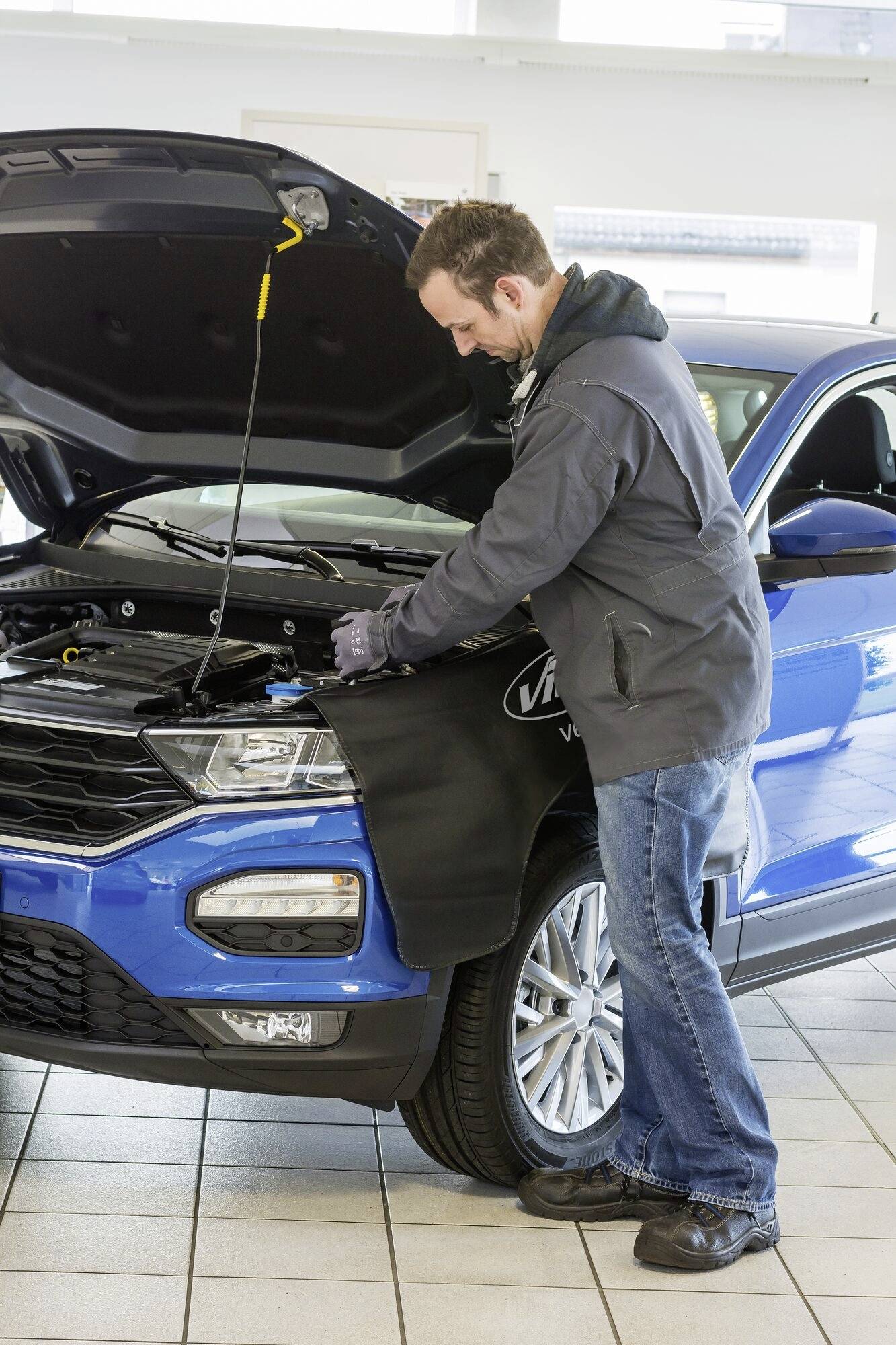 Mężczyzna pracuje w warsztacie przy niebieskim samochodzie z otwartą maską silnika.