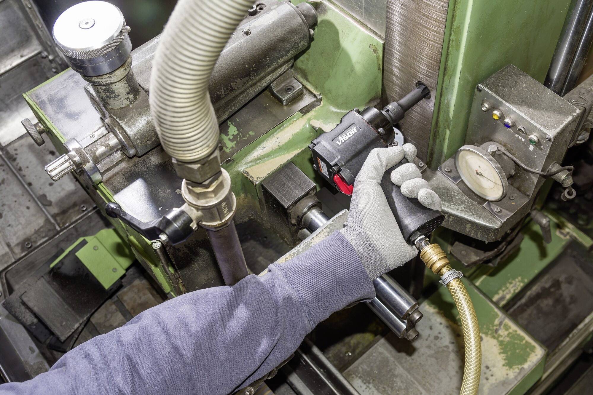 Osoba obsługuje przemysłową szlifierkę do obróbki elementu metalowego. Przyrząd pomiarowy wskazuje ciśnienie.