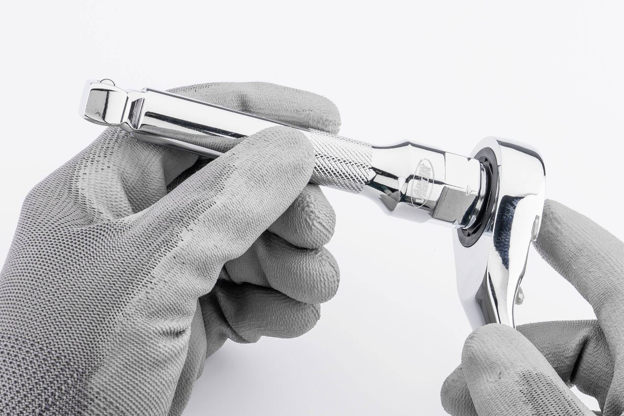 Osoba w szarych rękawiczkach trzyma chromowany klucz nastawny z grzechotką, z fokusem na narzędzie.