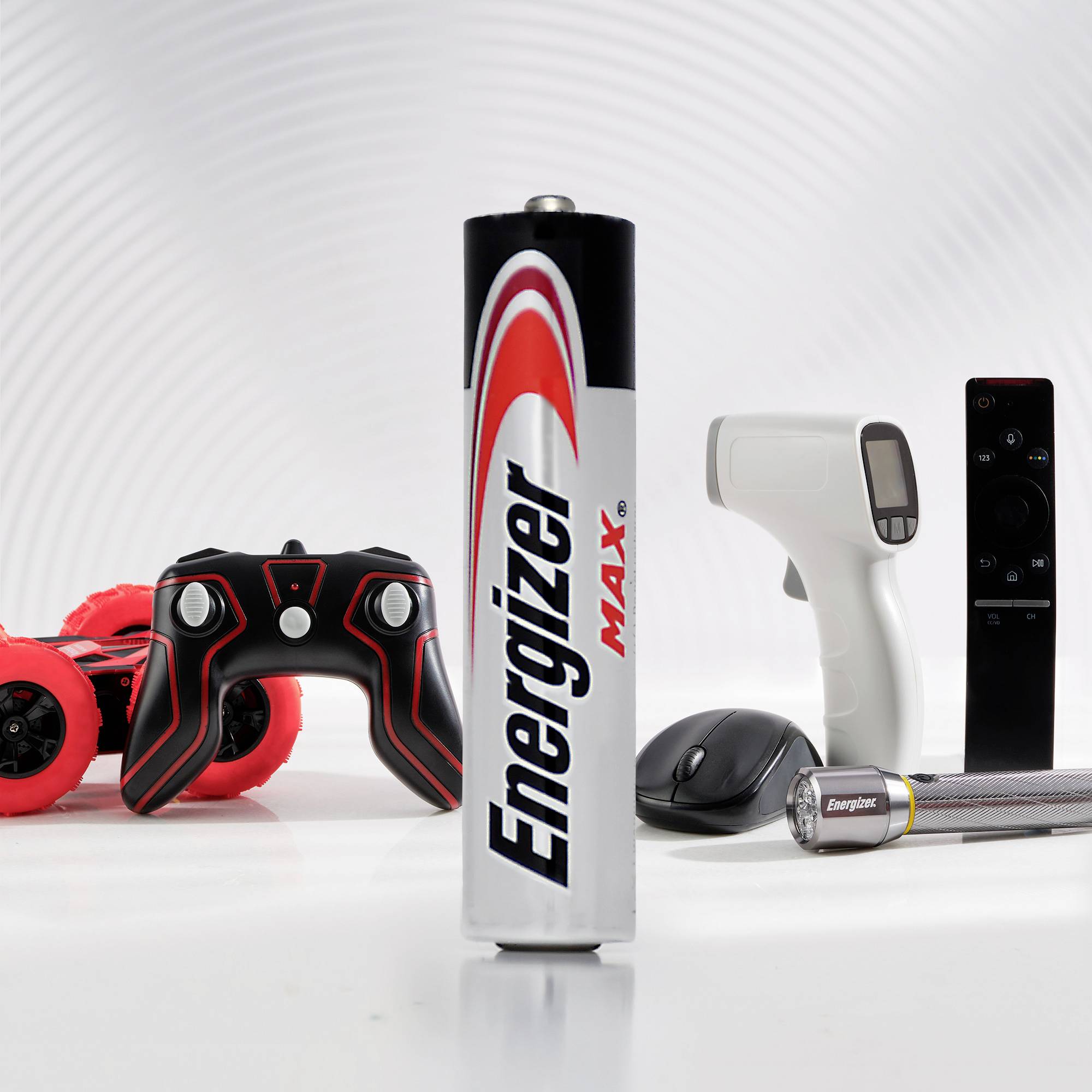 Bateria Energizer znajduje się na pierwszym planie. W tle widoczne są czerwony samochód zdalnie sterowany, pilot, mysz komputerowa oraz laserowy termometr.