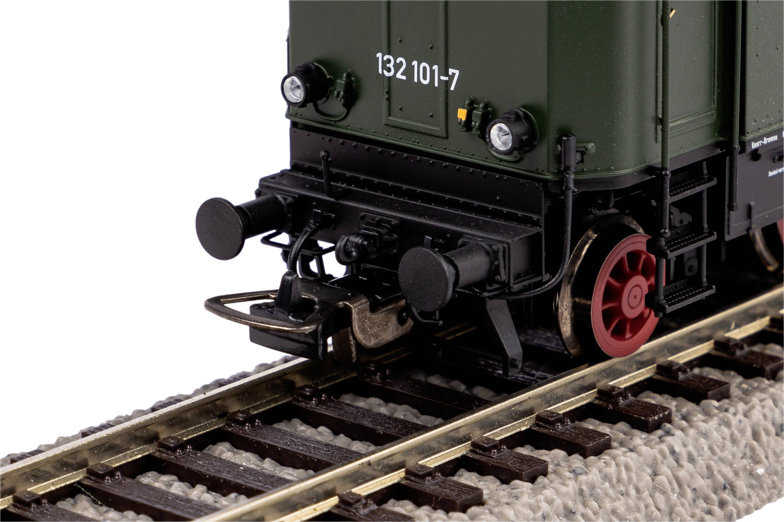 Wagon z siecią trakcyjną kolejki modelarskiej widziany z góry na torach, z czerwonym okablowaniem i szarą obudową.