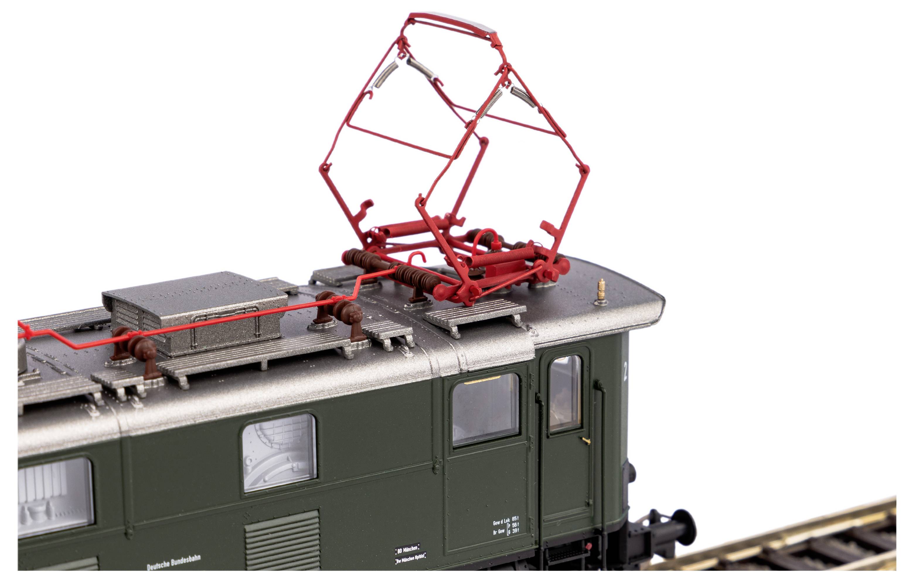 Elektryczny pociąg modelarski z zielonym korpusem i czerwonym pantografem. Wykazuje precyzyjne detale i jest umieszczony na torach.