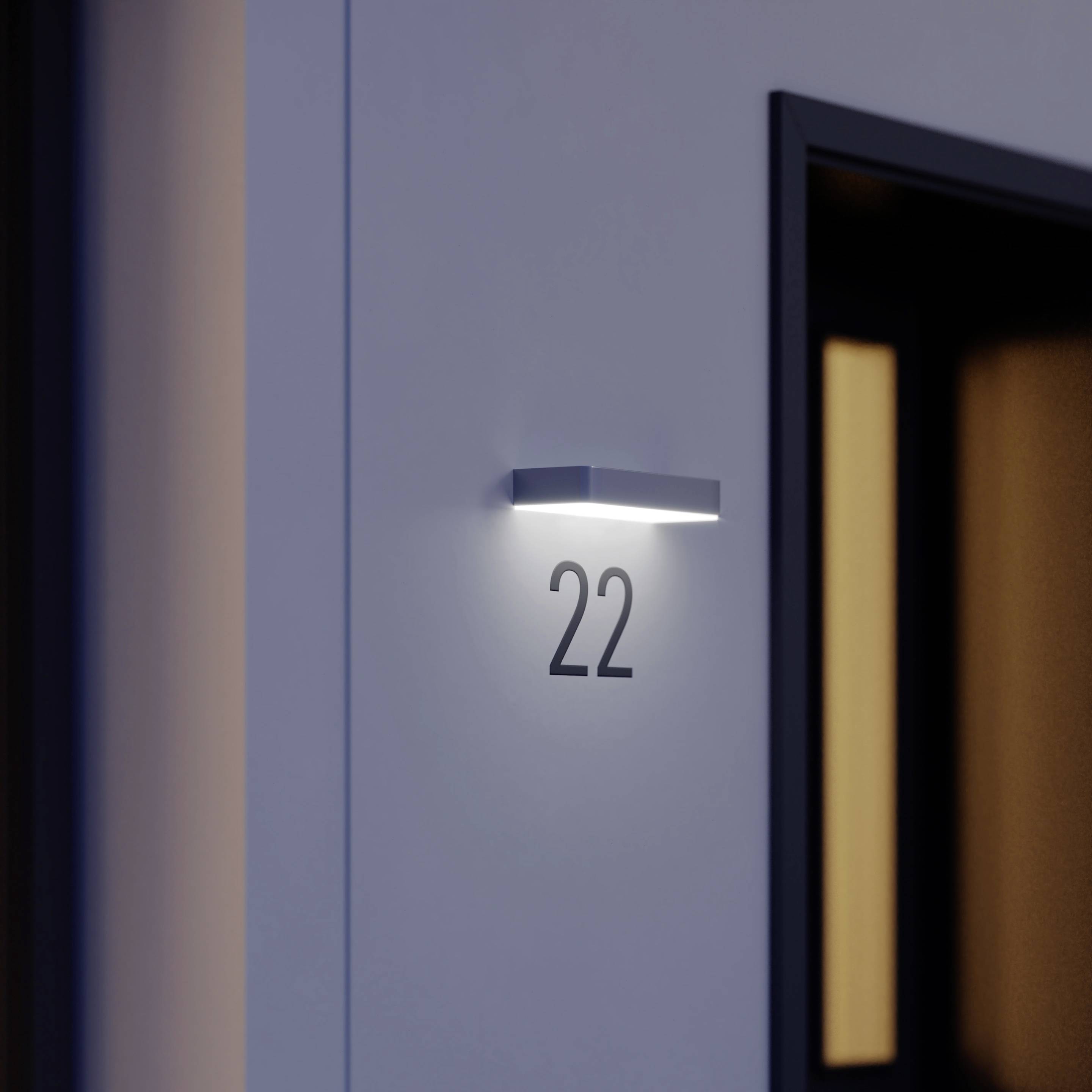Numer pokoju 22, oświetlony przez kinkiet ścienny, obok drzwi budynku.