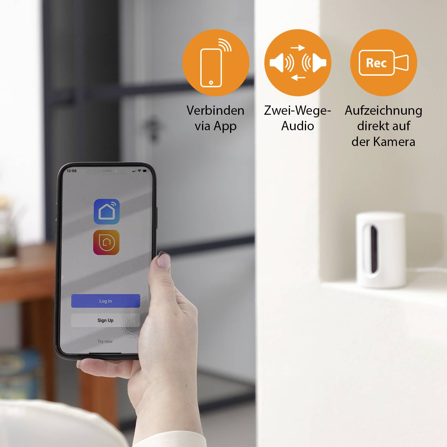 Dłoń trzyma smartfon z ekranem logowania aplikacji. W tle znajduje się kamera. Symbole przedstawiają połączenie z aplikacją, dwukierunkowy dźwięk oraz nagrywanie wideo.