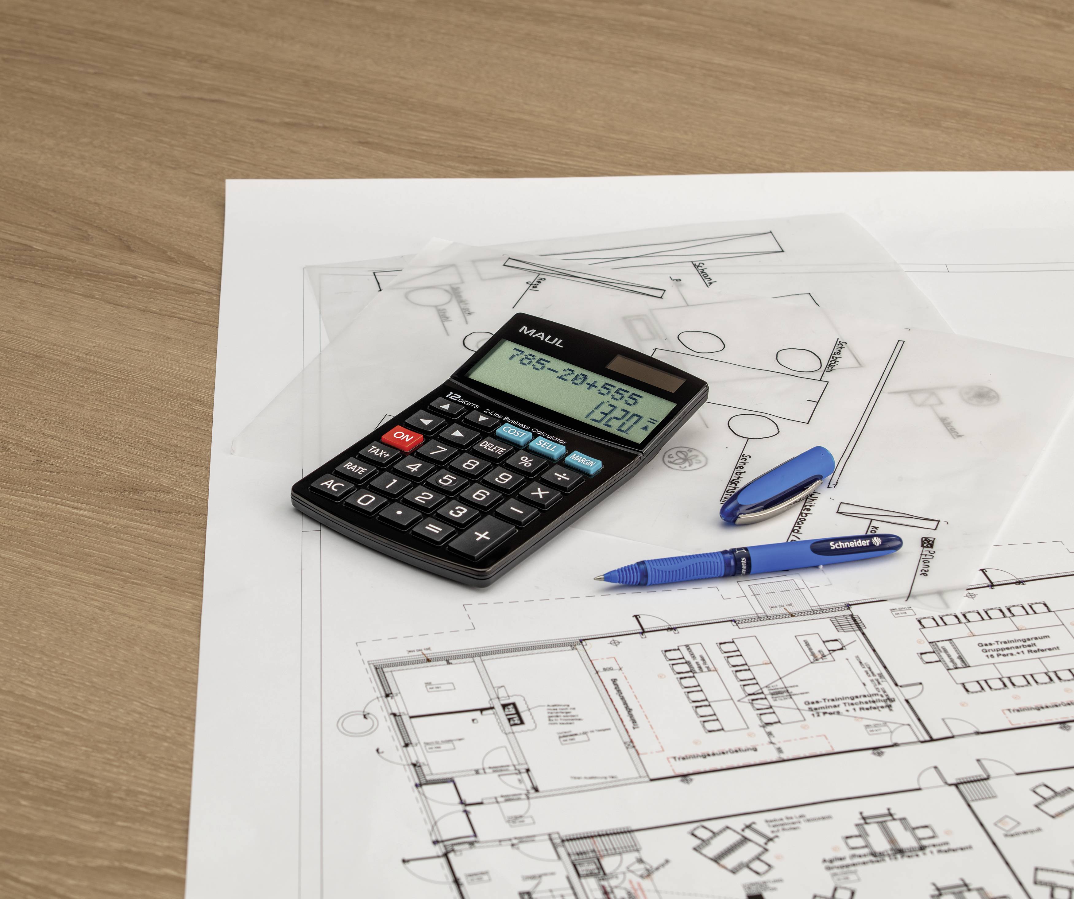 Stół z planem architektonicznym, kalkulatorem i piórami symbolizuje planowanie i kalkulację w budownictwie.