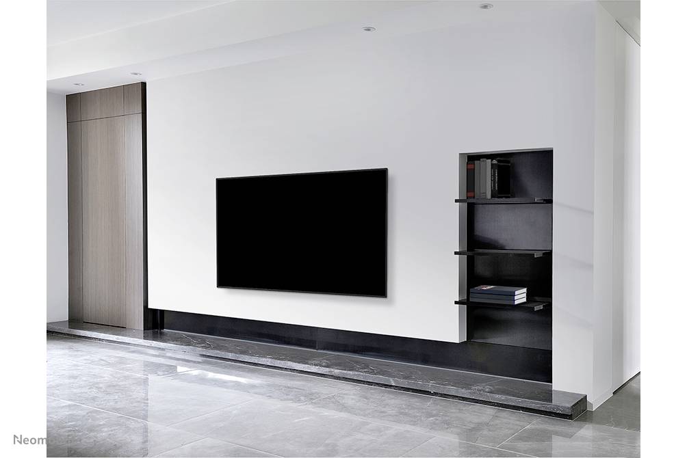 Nowoczesny salon z dużym, czarnym telewizorem plazmowym na białej ścianie, obok którego stoi regał z książkami.