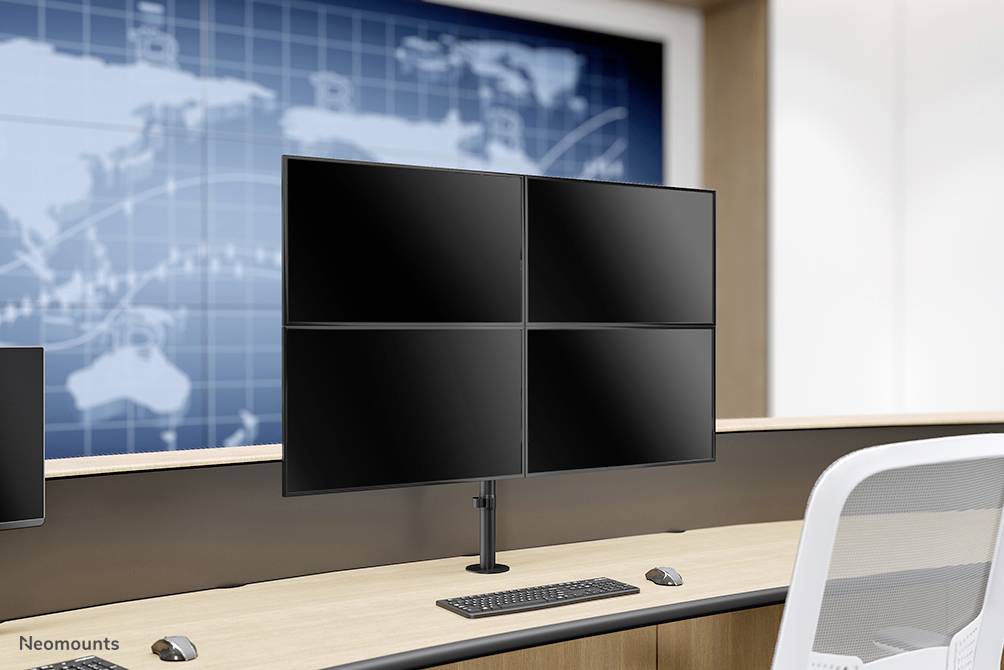 Biuro z biurkiem, na którym stoi podstawka pod monitor z czterema monitorami. Na tle ściany widać mapę świata.