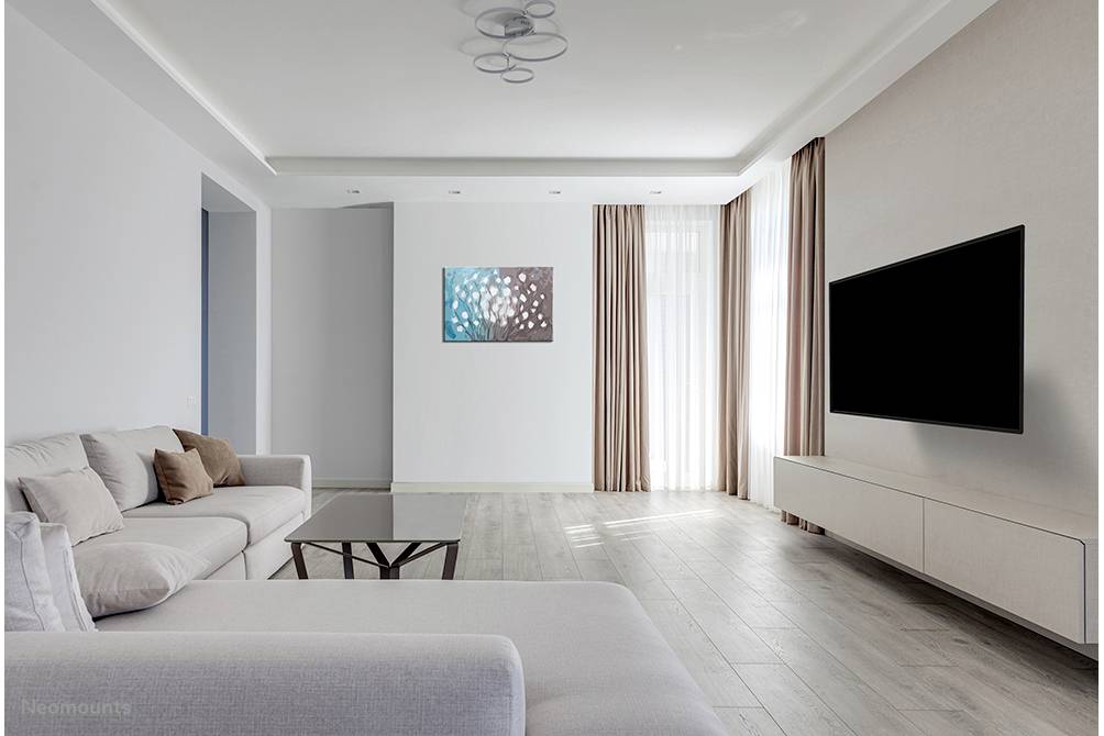 Nowoczesny salon z jasną sofą, stolikiem kawowym i dużym telewizorem LCD zamontowanym na ścianie. Okna od podłogi do sufitu z zasłonami.