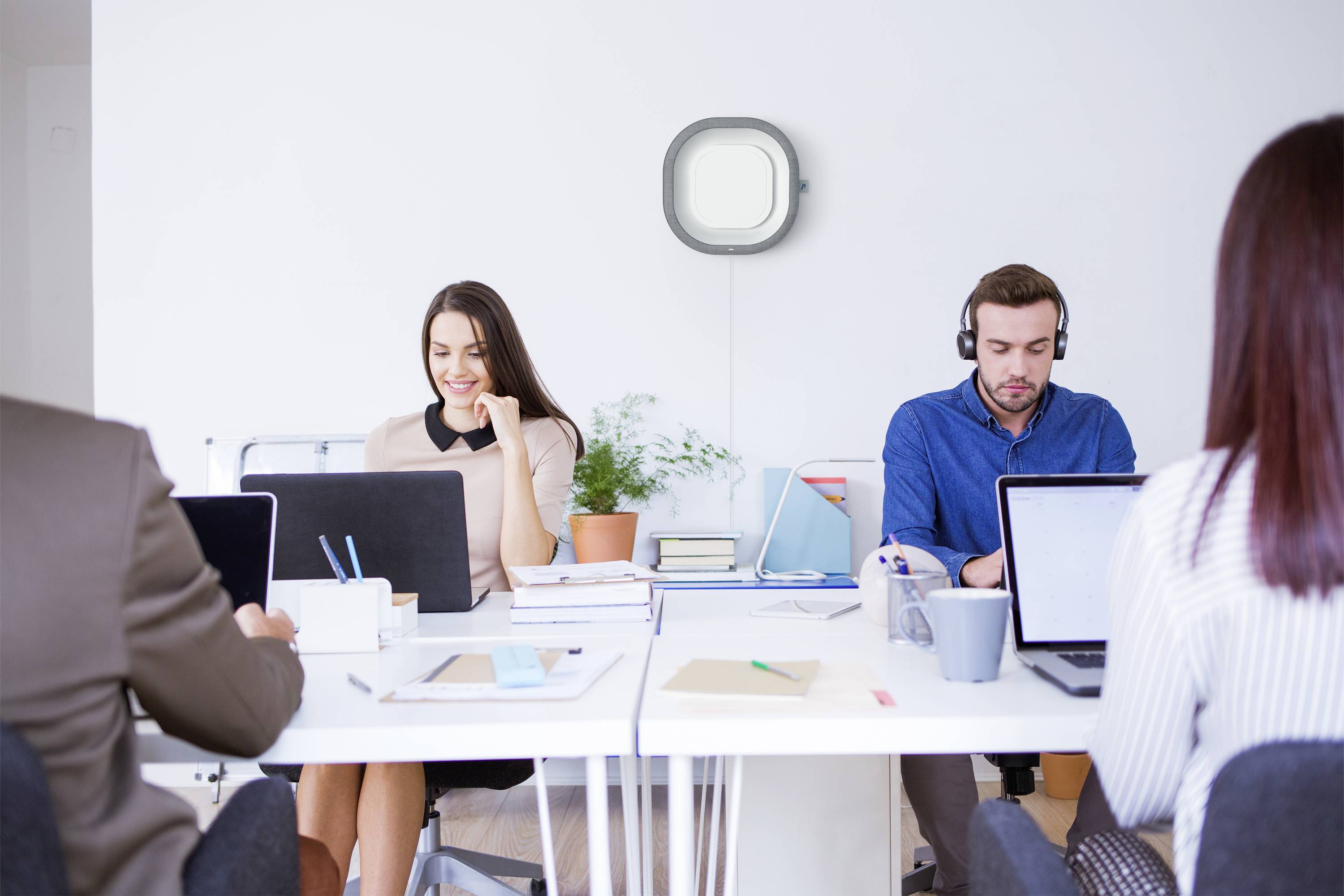 Zespół pracuje w nowoczesnym biurze. Dwie osoby noszą słuchawki i pracują na laptopach. Jeden z pracowników rozmawia przez telefon.