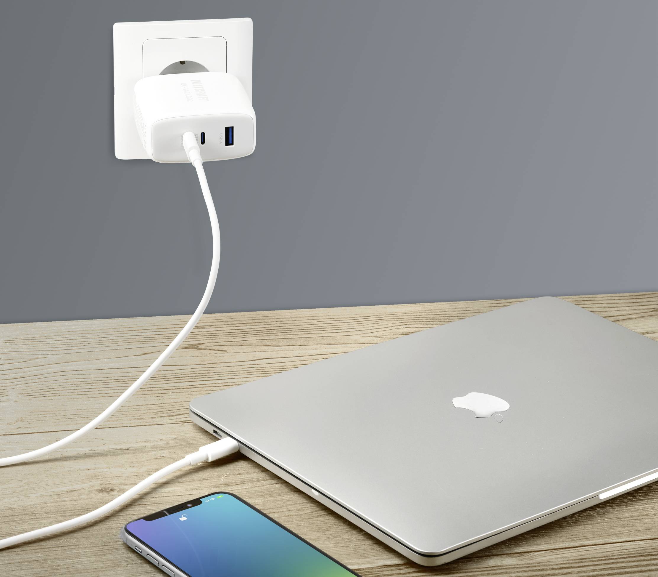 Smartfon i laptop leżą na stole. Oba są podłączone do ładowarki, która jest włożona do gniazdka ściennego.