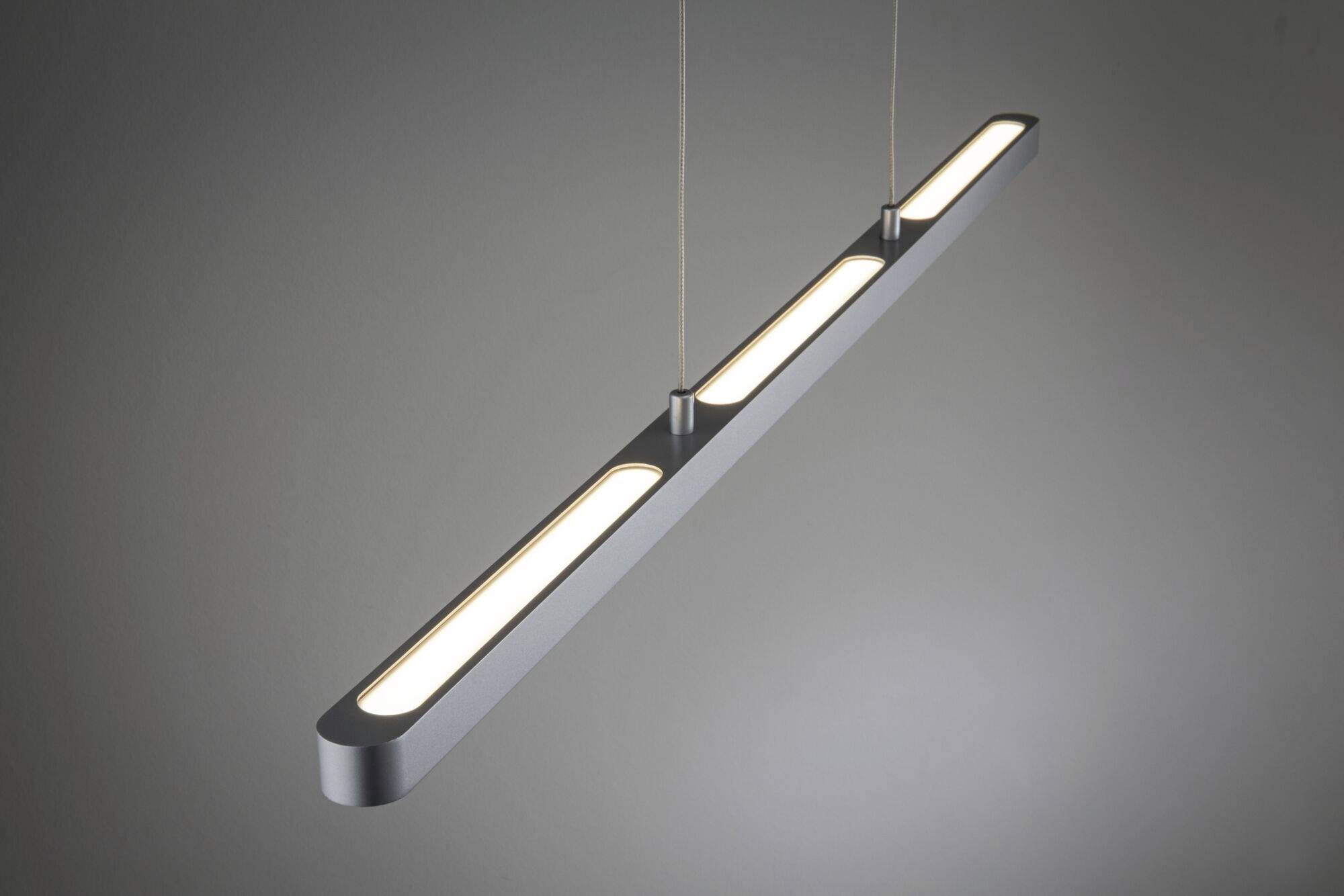 Nowoczesna, podłużna lampa wisząca LED o prostym, matowym designie, zawieszona poziomo w szarym pomieszczeniu, emituje ciepłe światło.