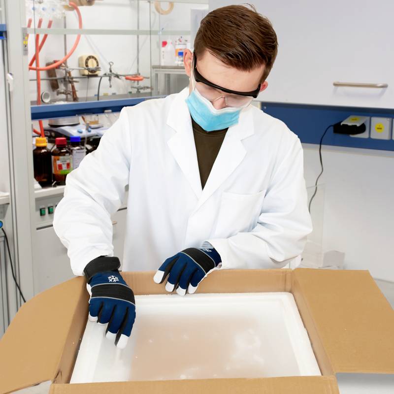 Naukowiec w laboratorium nosi okulary ochronne i maskę, pracując nad projektem w rękawicy ochronnej wewnątrz boksu.