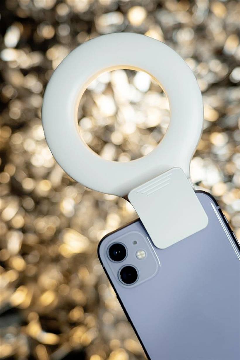 Smartfon z zamocowanym pierścieniem świetlnym na pierwszym planie, rozmyty, błyszczący tło.