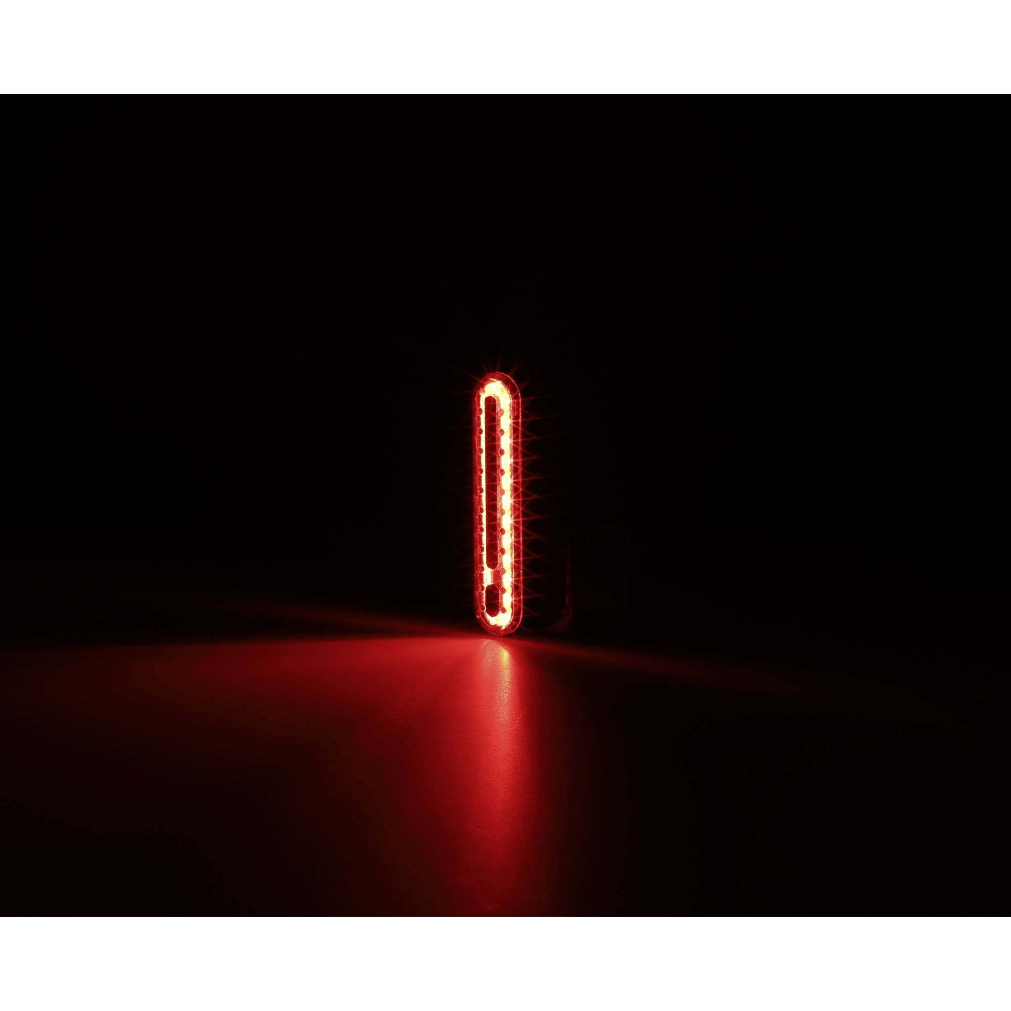 Czerwone tylne światło pojazdu świeci w ciemności, wyraźnie odcinając się od czarnego tła.