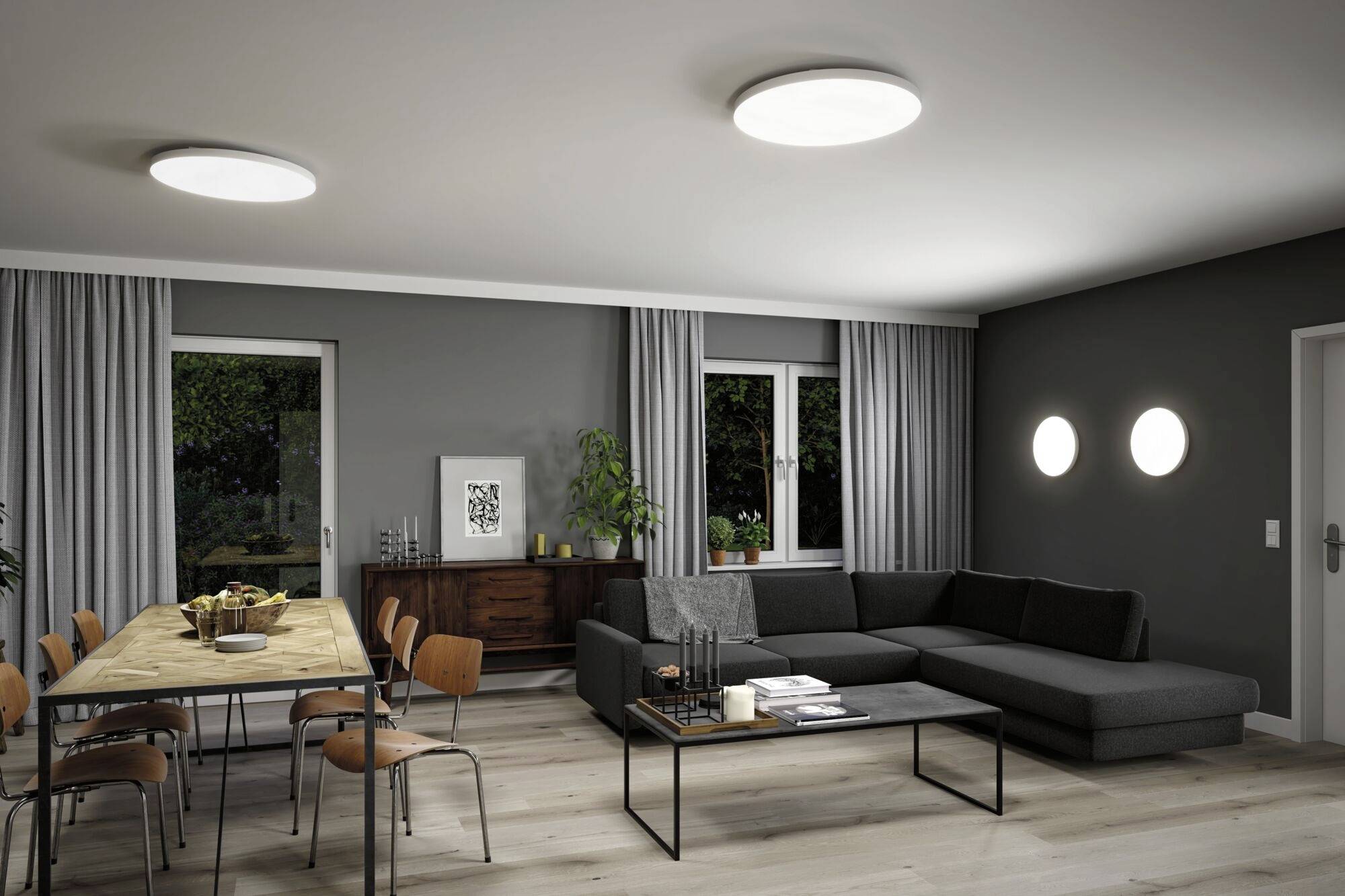 Nowoczesny salon z szarymi ścianami, sofą w kształcie litery L, stołem jadalnianym z krzesłami i kilkoma roślinami. Jasne oświetlenie.