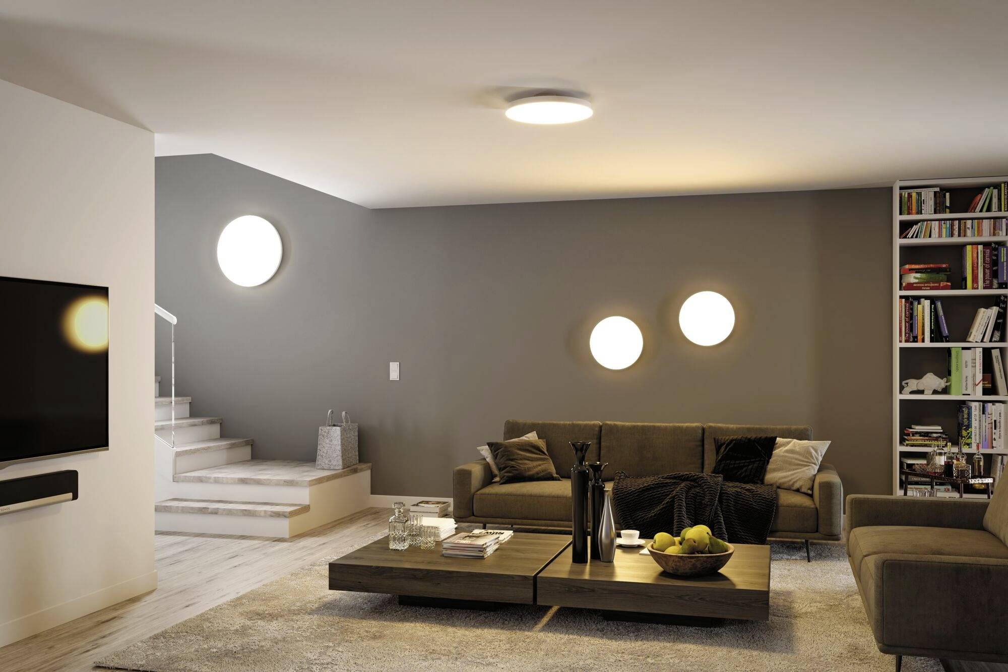 Nowoczesny salon z szarymi ścianami i brązową sofą. Stolik kawowy z dekoracjami stoi pośrodku. W tle widoczne są schody.