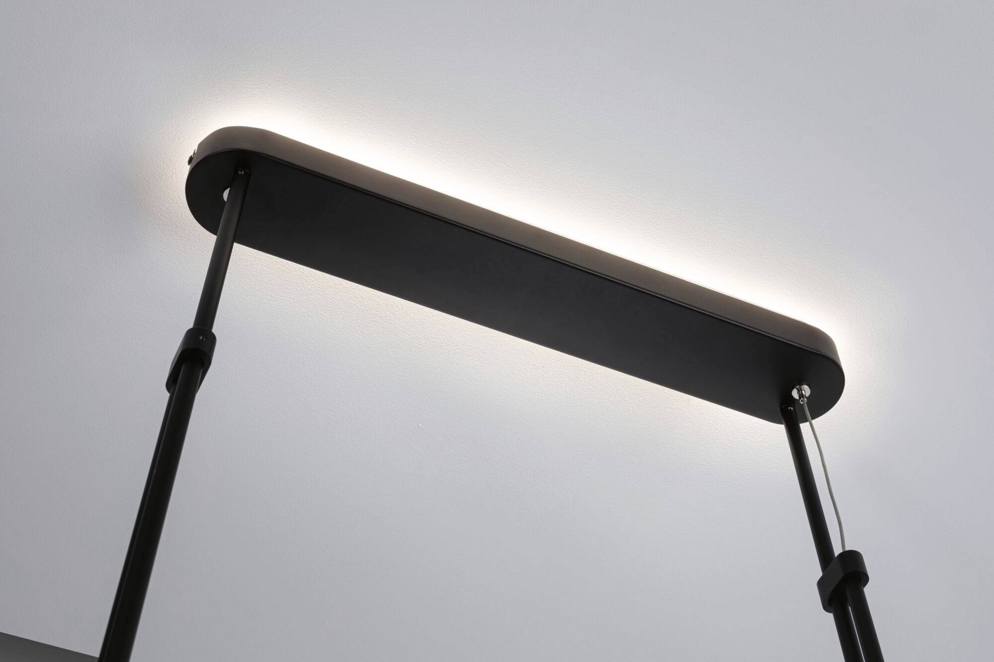 Lampa wisząca o prostym, prostokątnym kształcie, zamocowana przy suficie. U góry delikatnie świeci światło.
