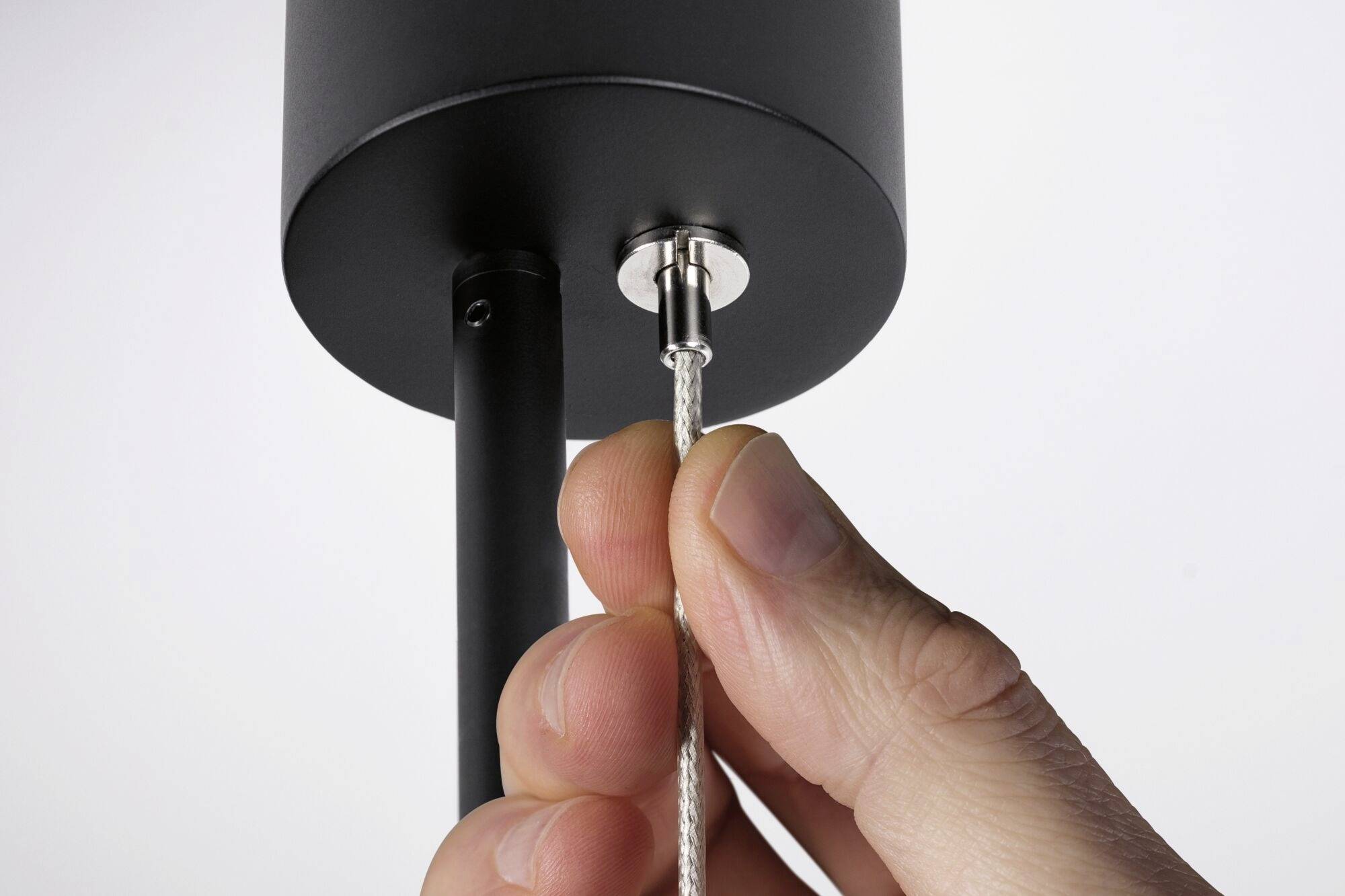 Jedna ręka ciągnie za pleciony kabel podłączony do czarnego, cylindrycznego urządzenia.